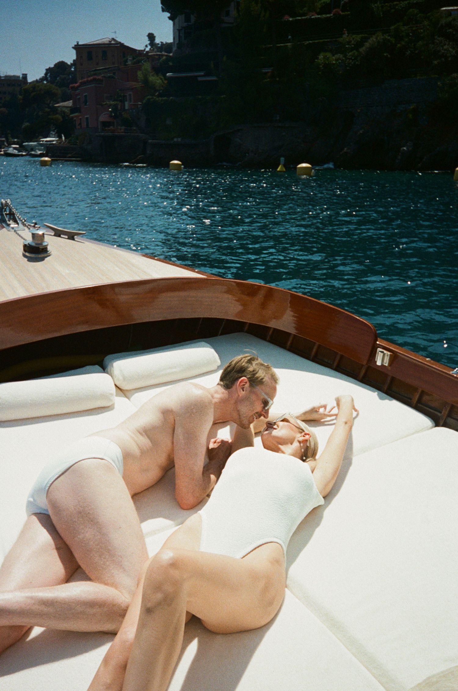 Romantic couple kissing on wooden boat deck with turquoise Italian Riviera waters behind them.