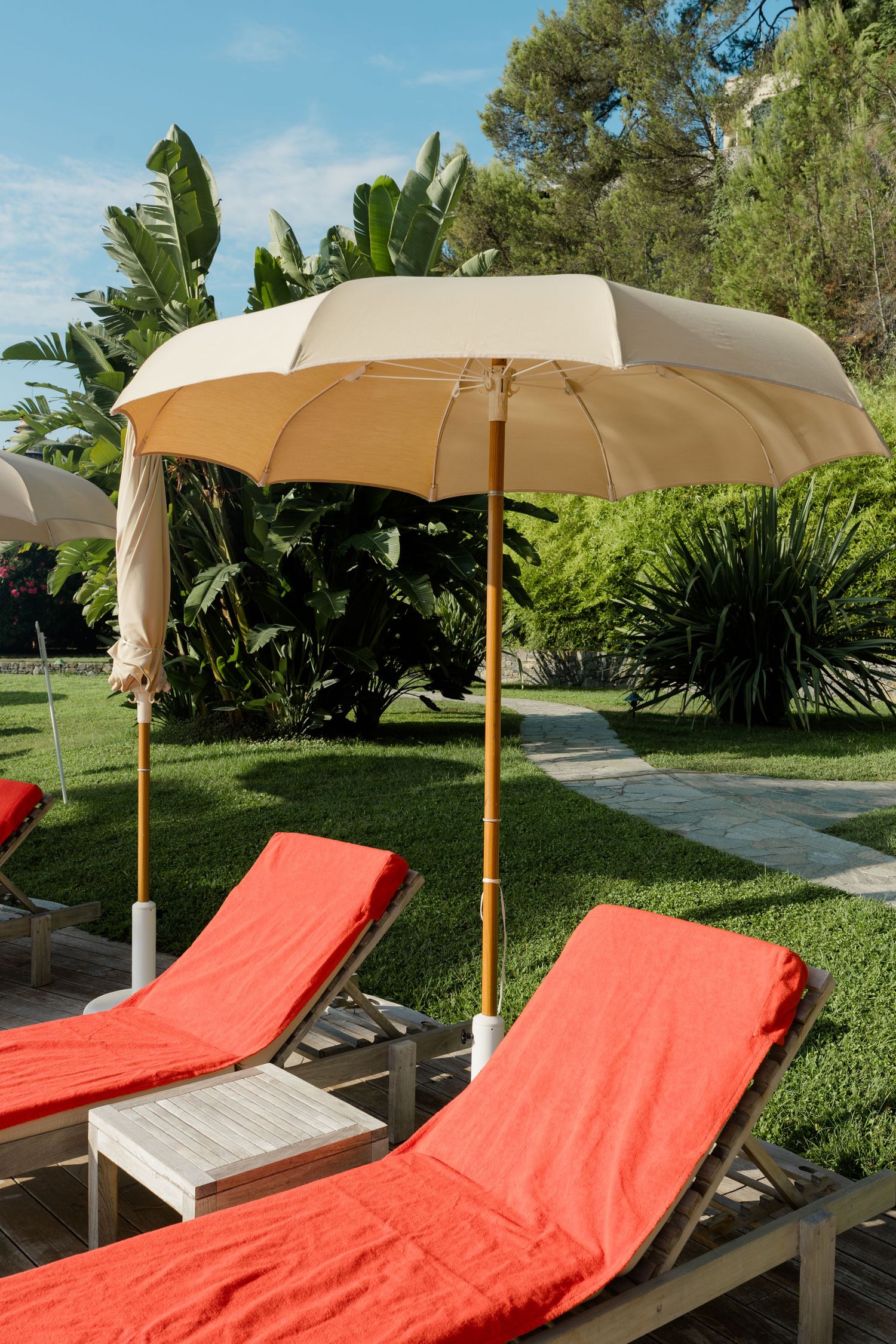 Red lounge chairs under a beige umbrella on a lush green lawn at a luxury resort.