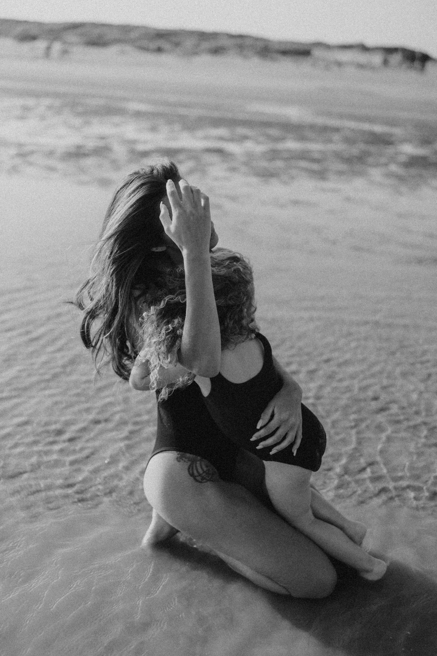 Black and white photo of people sitting and playing in wet sand at the beach.