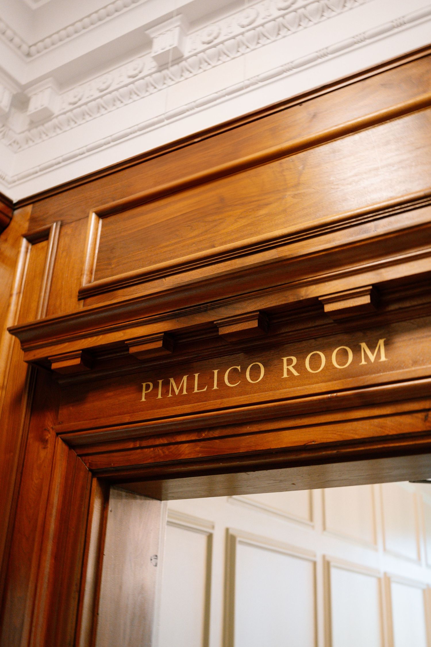 Elegant wooden doorway entrance with 'Pimlico Room' text engraved above in a classic interior setting.