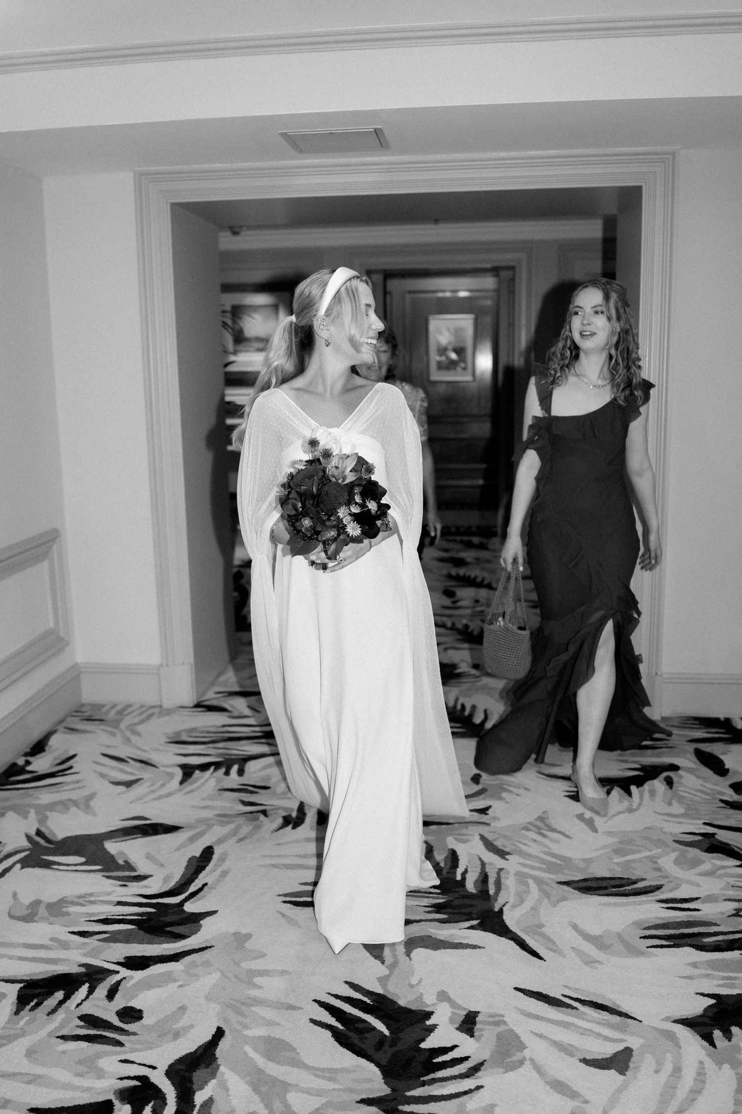 Wedding procession moving through luxurious hotel hallway with decorative carpeting.