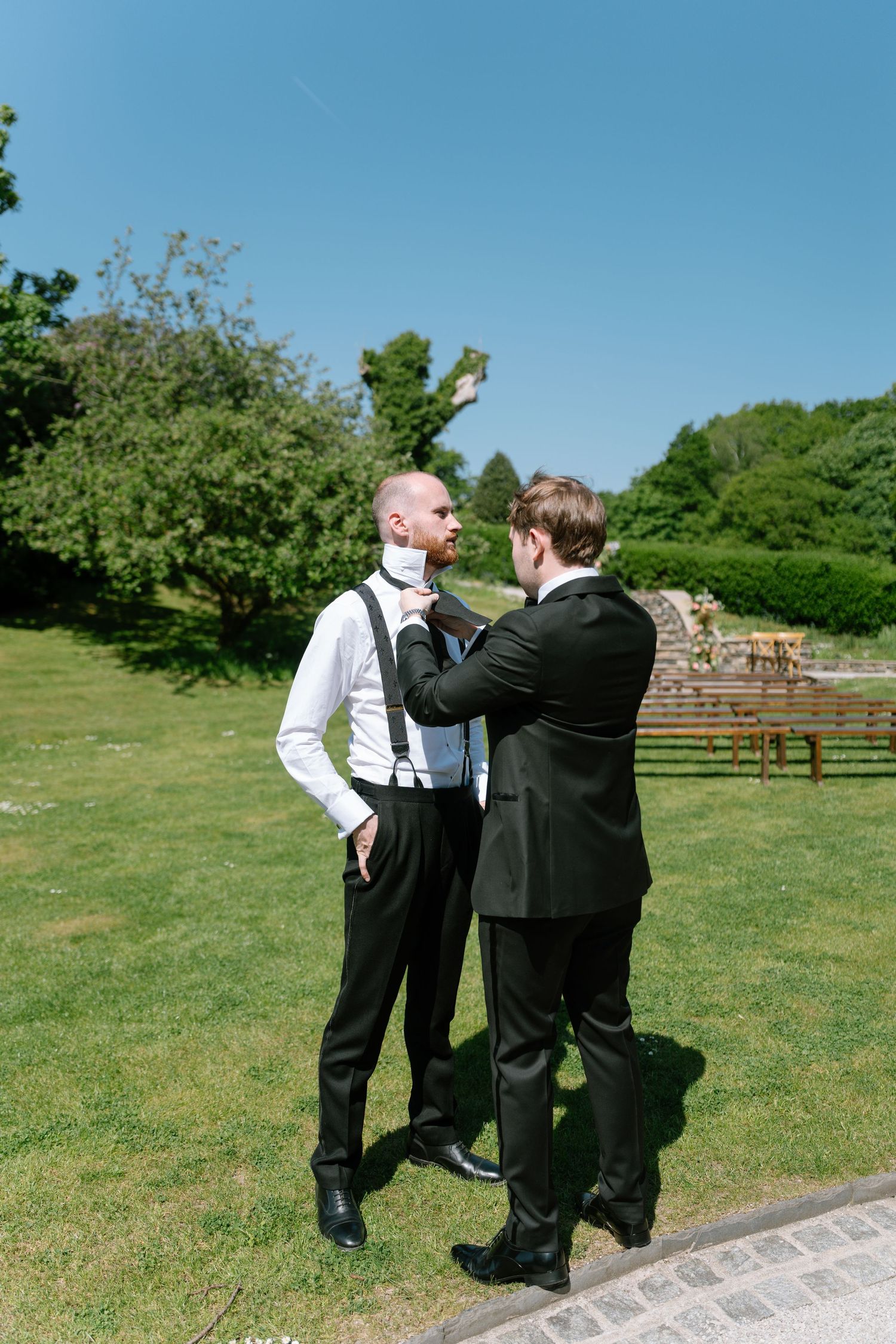People in formal attire standing on a path surrounded by green lawn and trees.