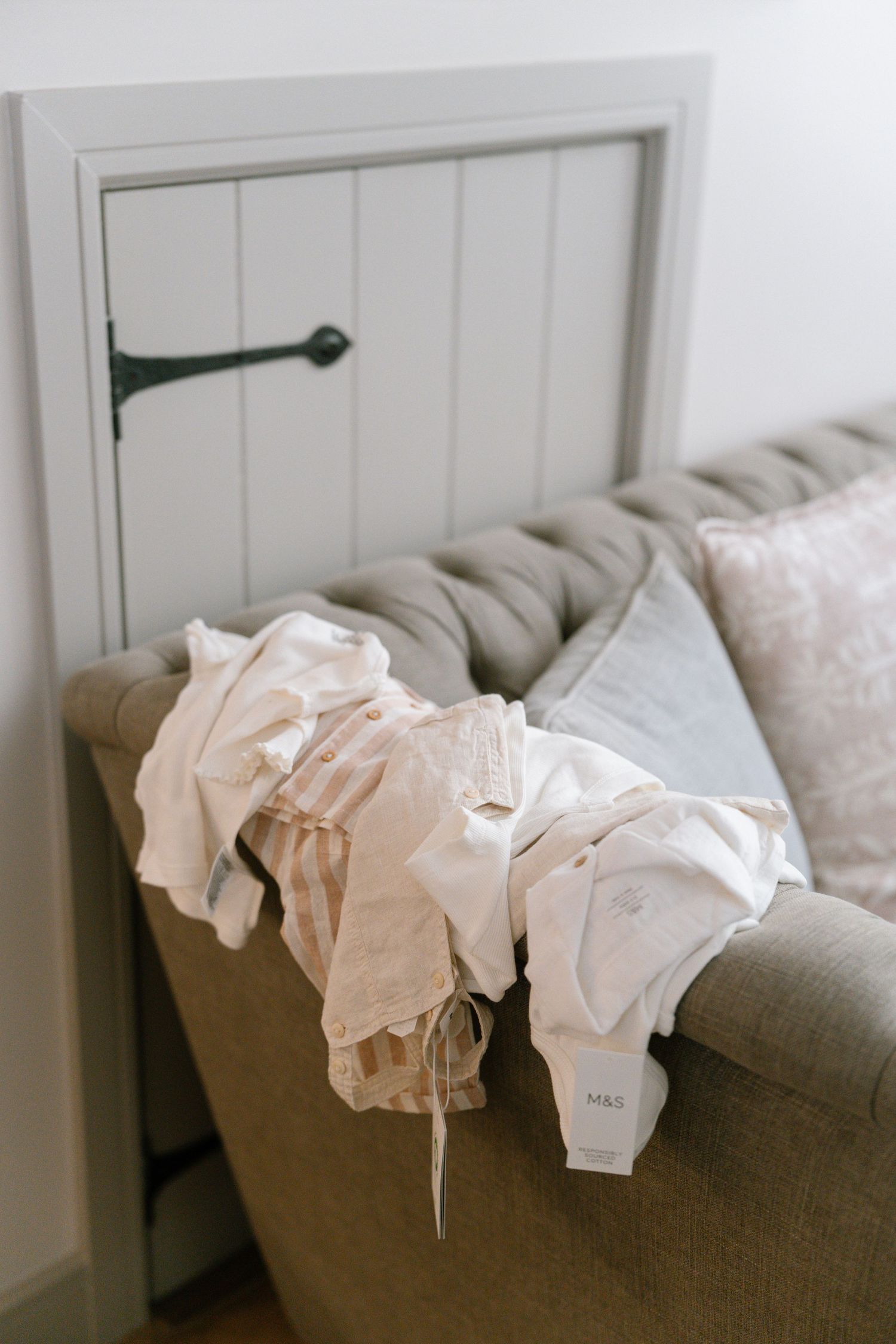 White baby clothes hanging to dry on a grey couch.