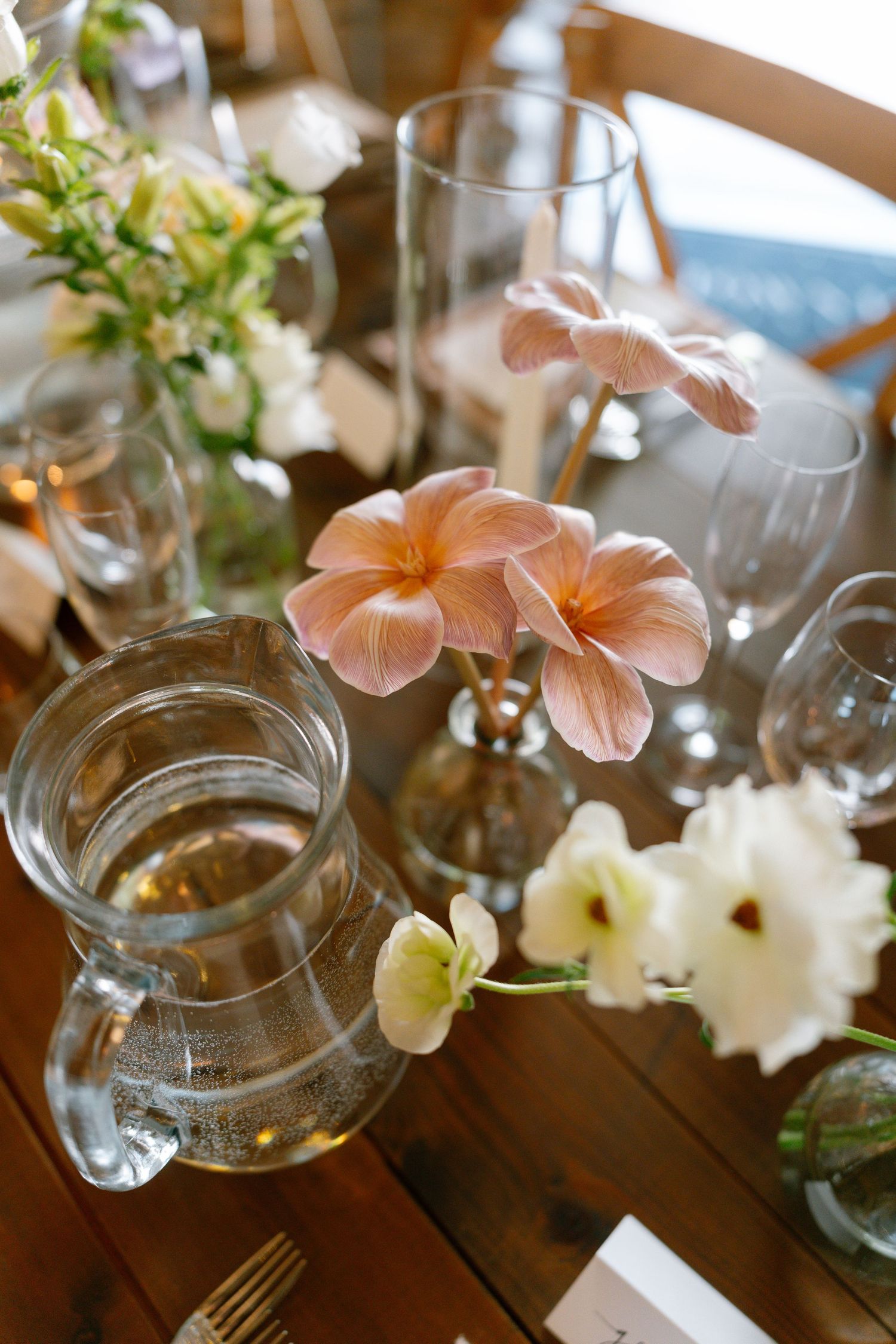Peach-colored flowers in glass vases arranged on a rustic wooden dining table with place settings.