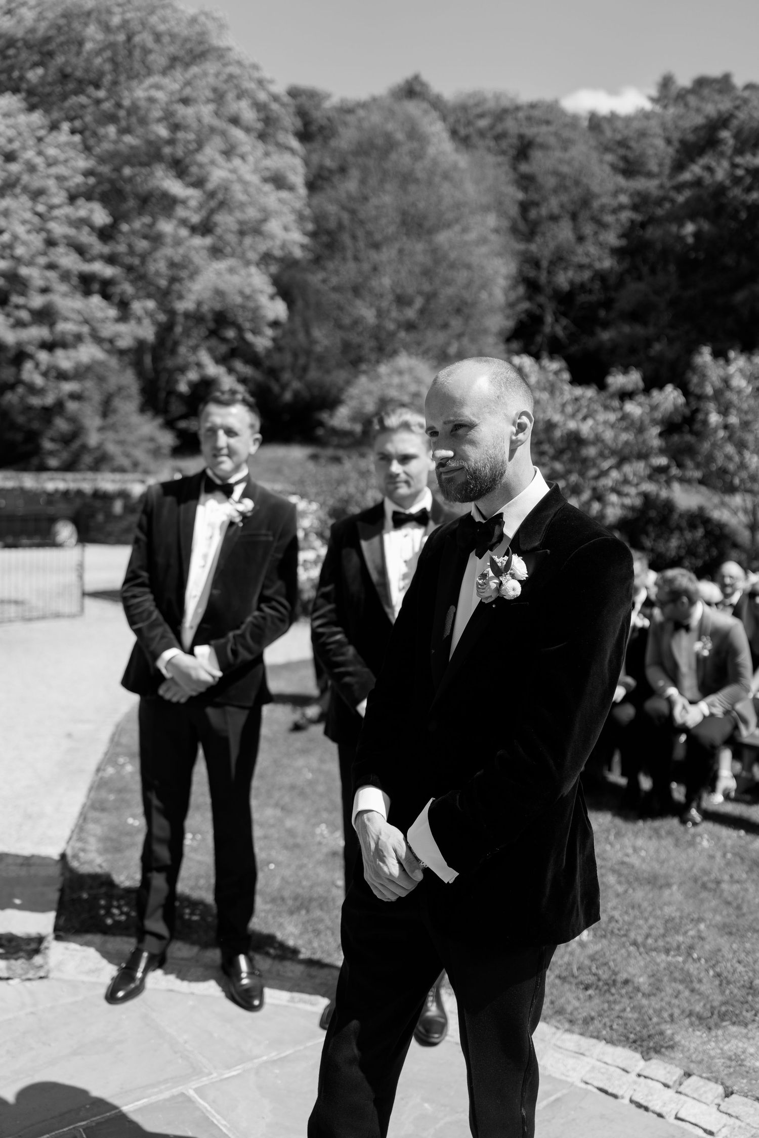 Groomsmen in tuxedos interact outdoors during a formal event.