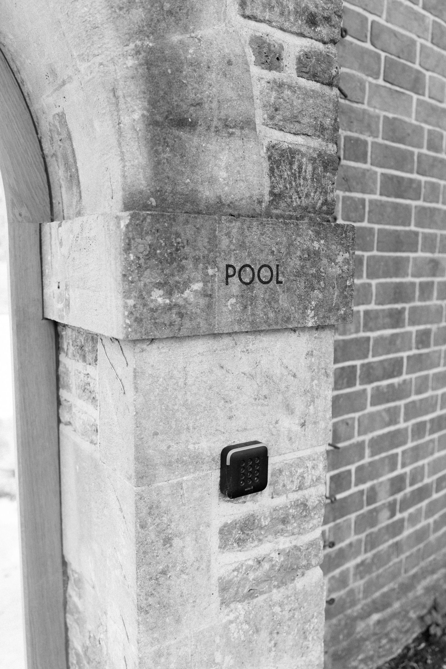 Black and white photo of a stone archway with a Pool sign and keypad entry at a wedding venue.
