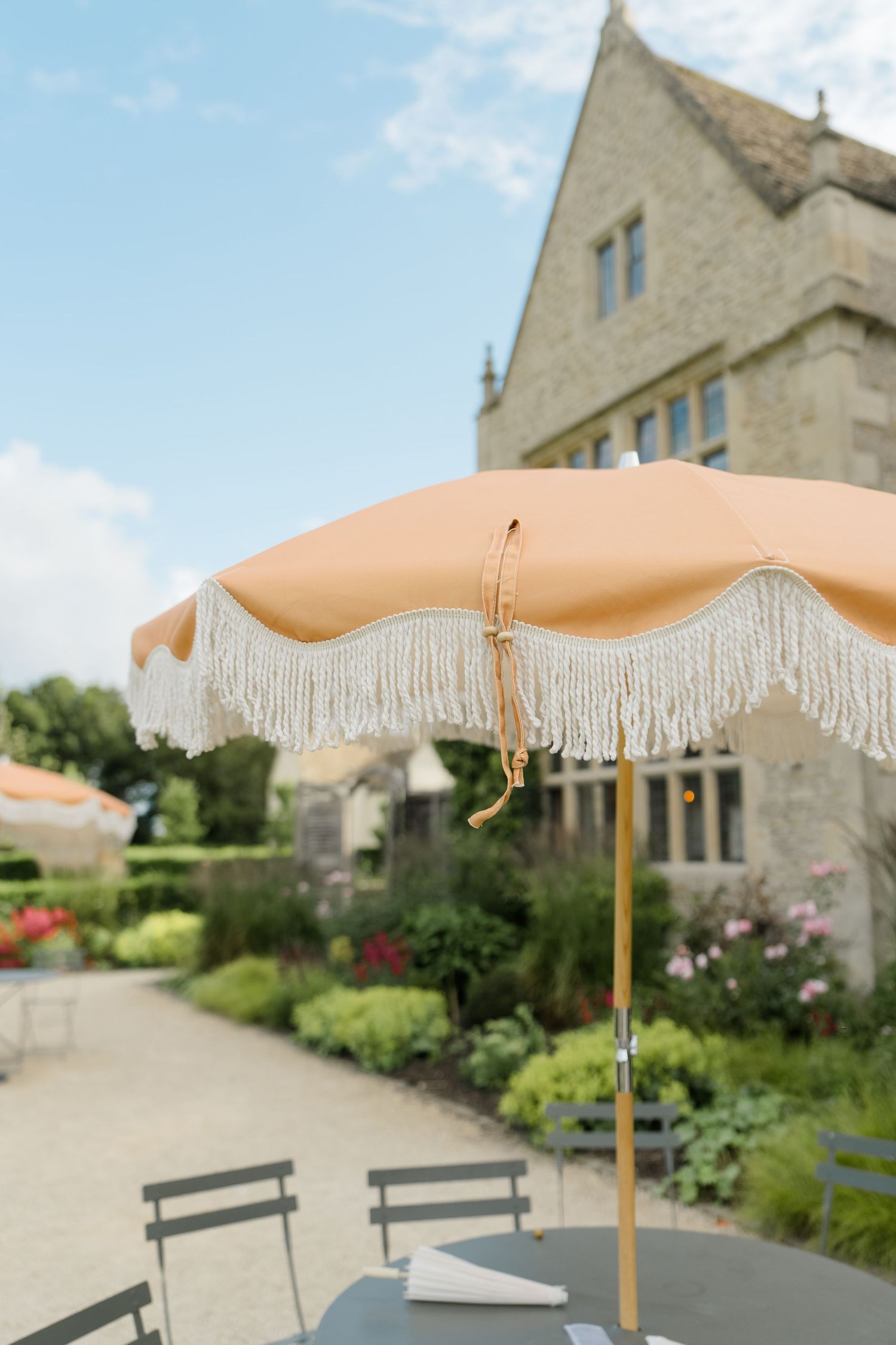Elegant fringed peach patio umbrella at a stone manor house garden venue.