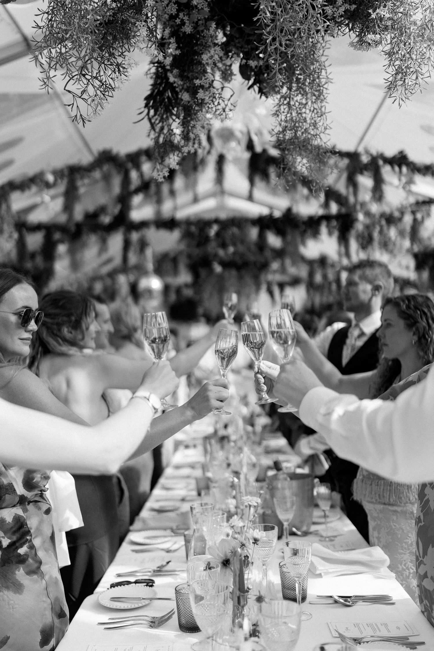 Guests raising champagne glasses during wedding toasts at an elegant outdoor reception.