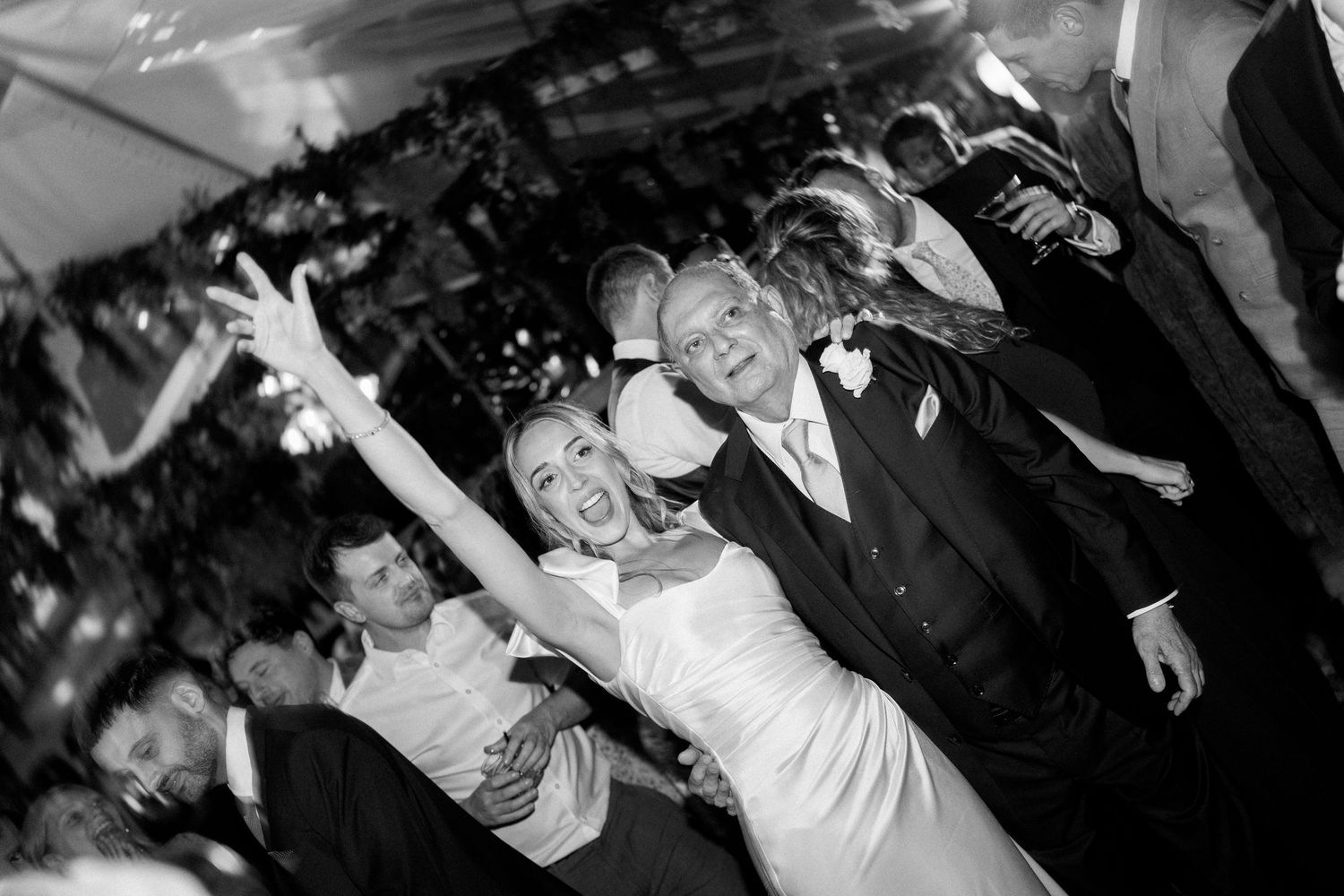 Black and white photo of wedding guests dancing with hands raised in celebration.