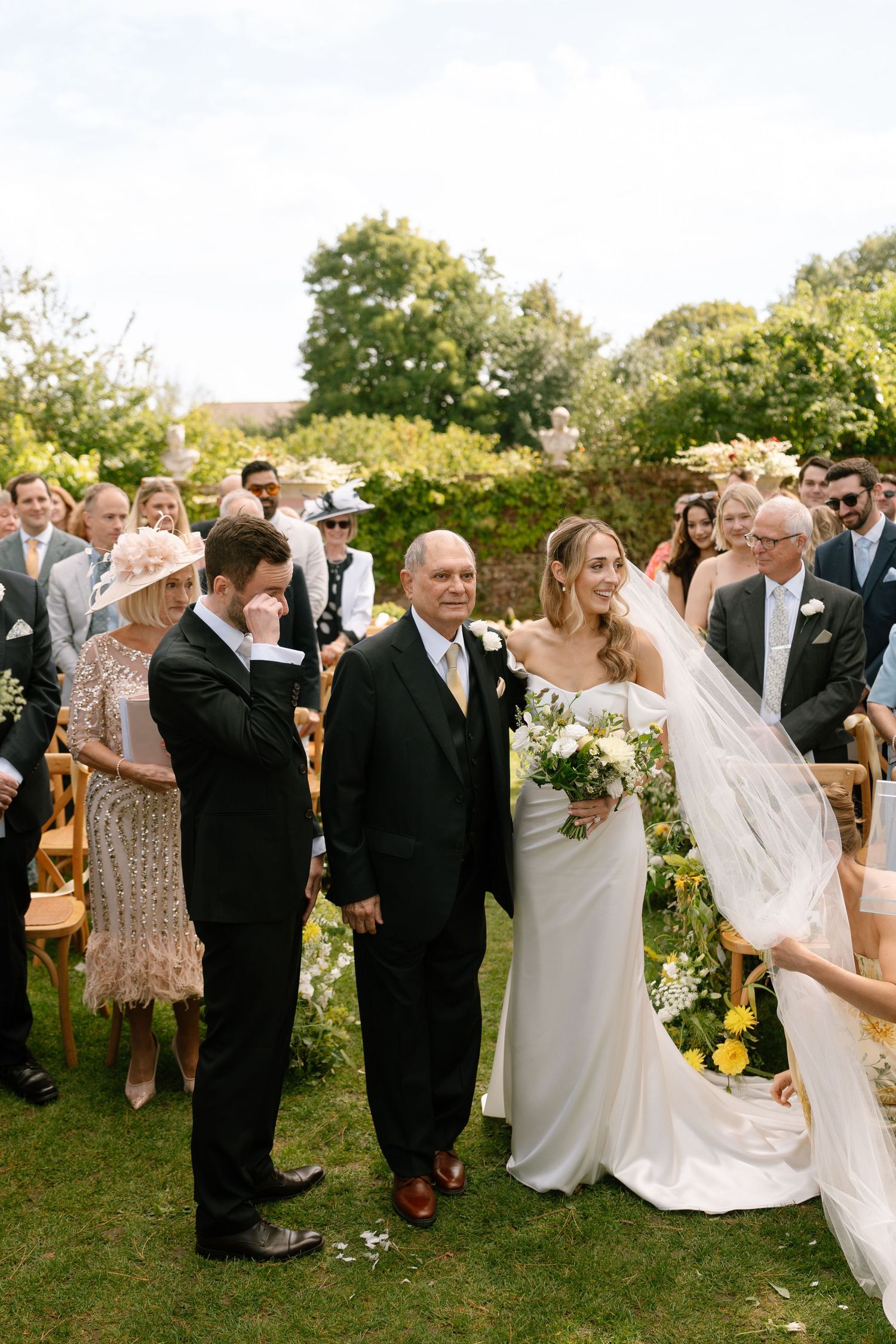Wedding party and guests mingle on a sunny lawn during an elegant outdoor celebration.
