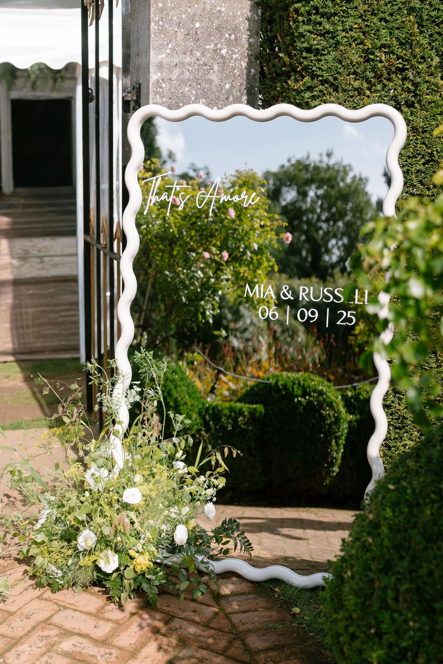 Decorative white frame displays wedding details against a garden backdrop.