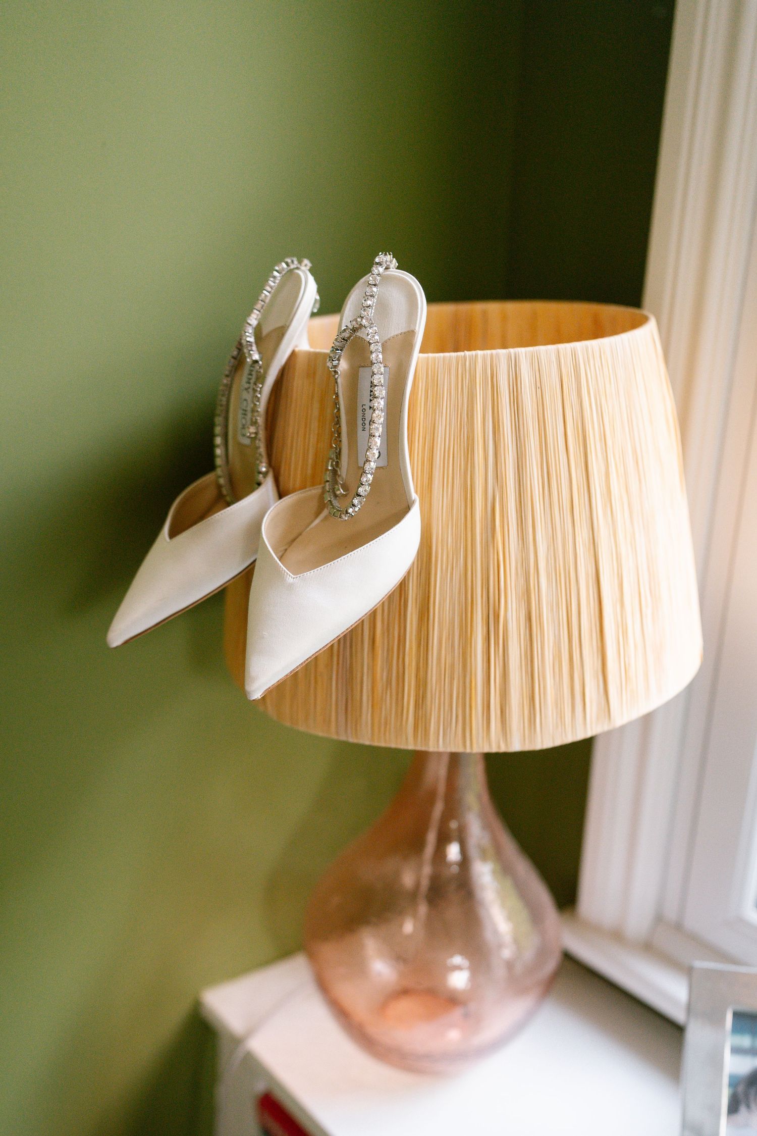 White bridal shoes displayed on a wooden pleated lampshade against a green background.