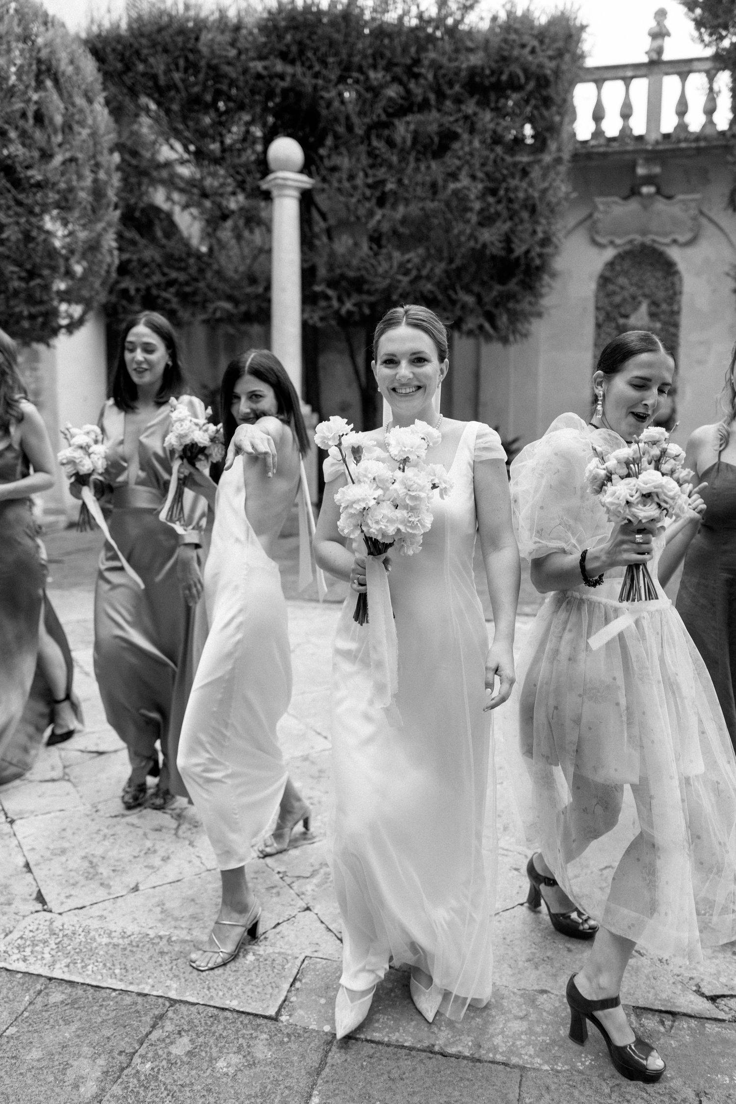 Black and white photo of wedding party walking through garden holding bouquets.