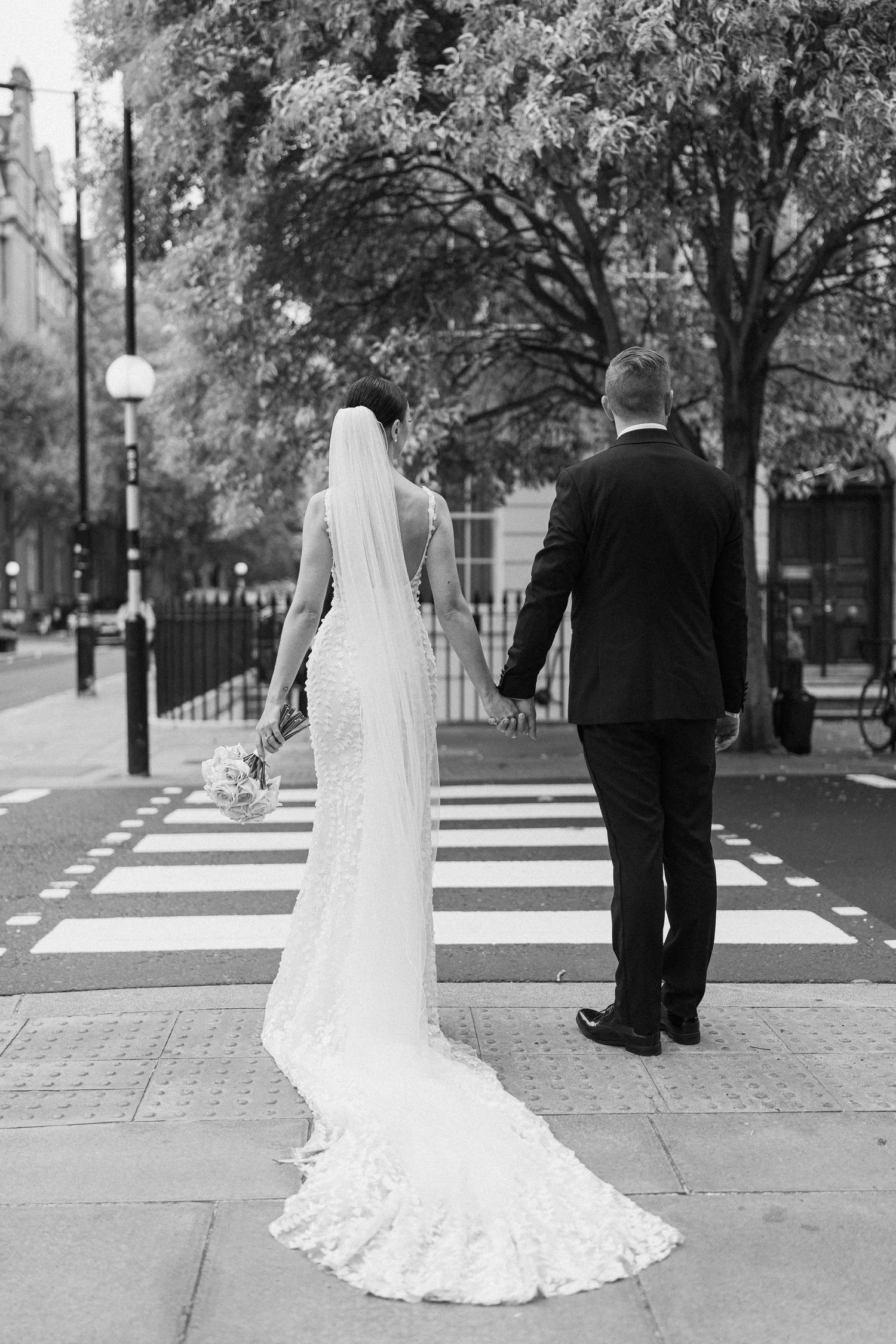 Black and white wedding photo of couple standing at crosswalk.