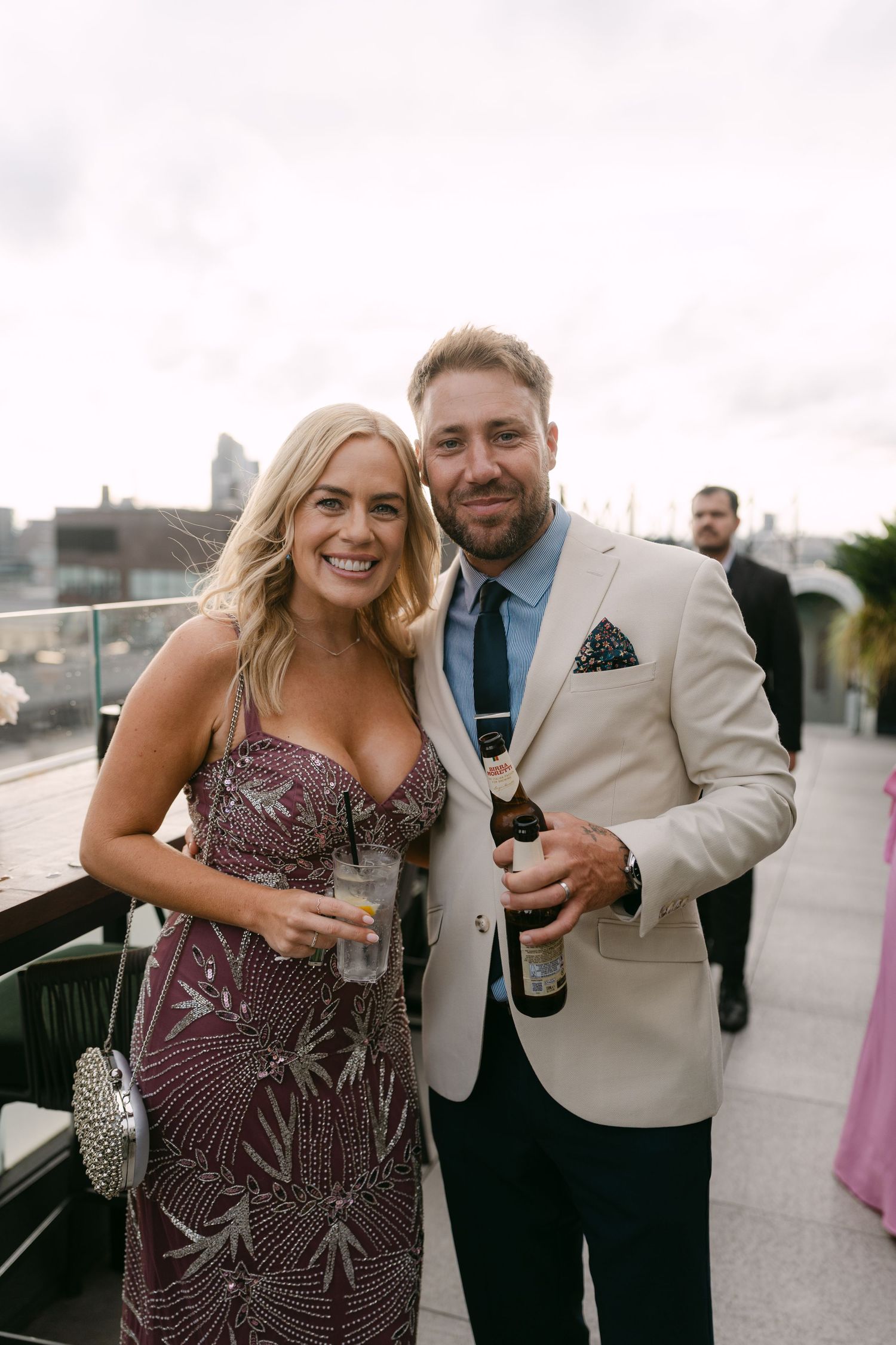 Wedding guests in formal attire sharing drinks and laughter at outdoor reception.
