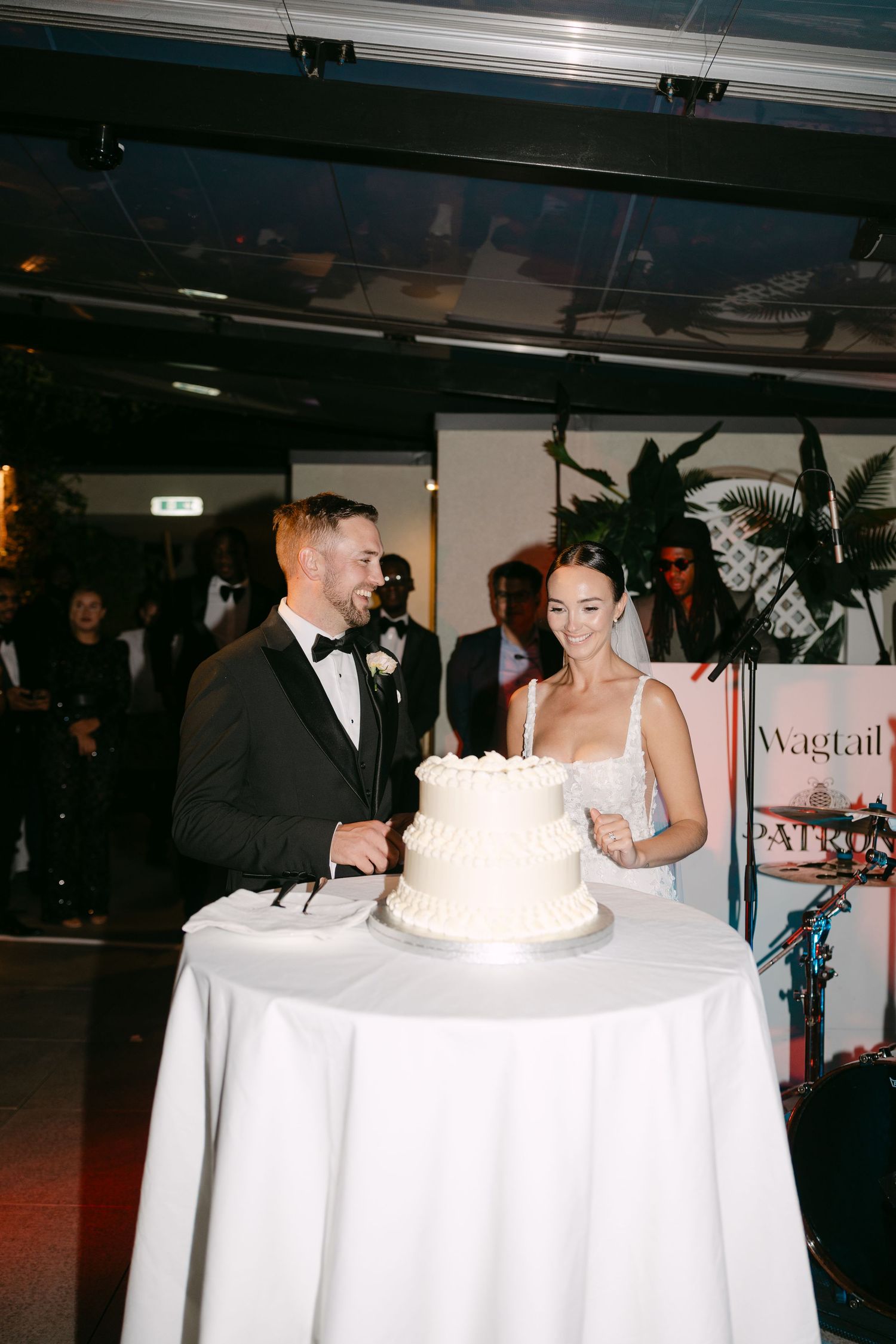 Newlyweds cutting their wedding cake together at an indoor reception venue.