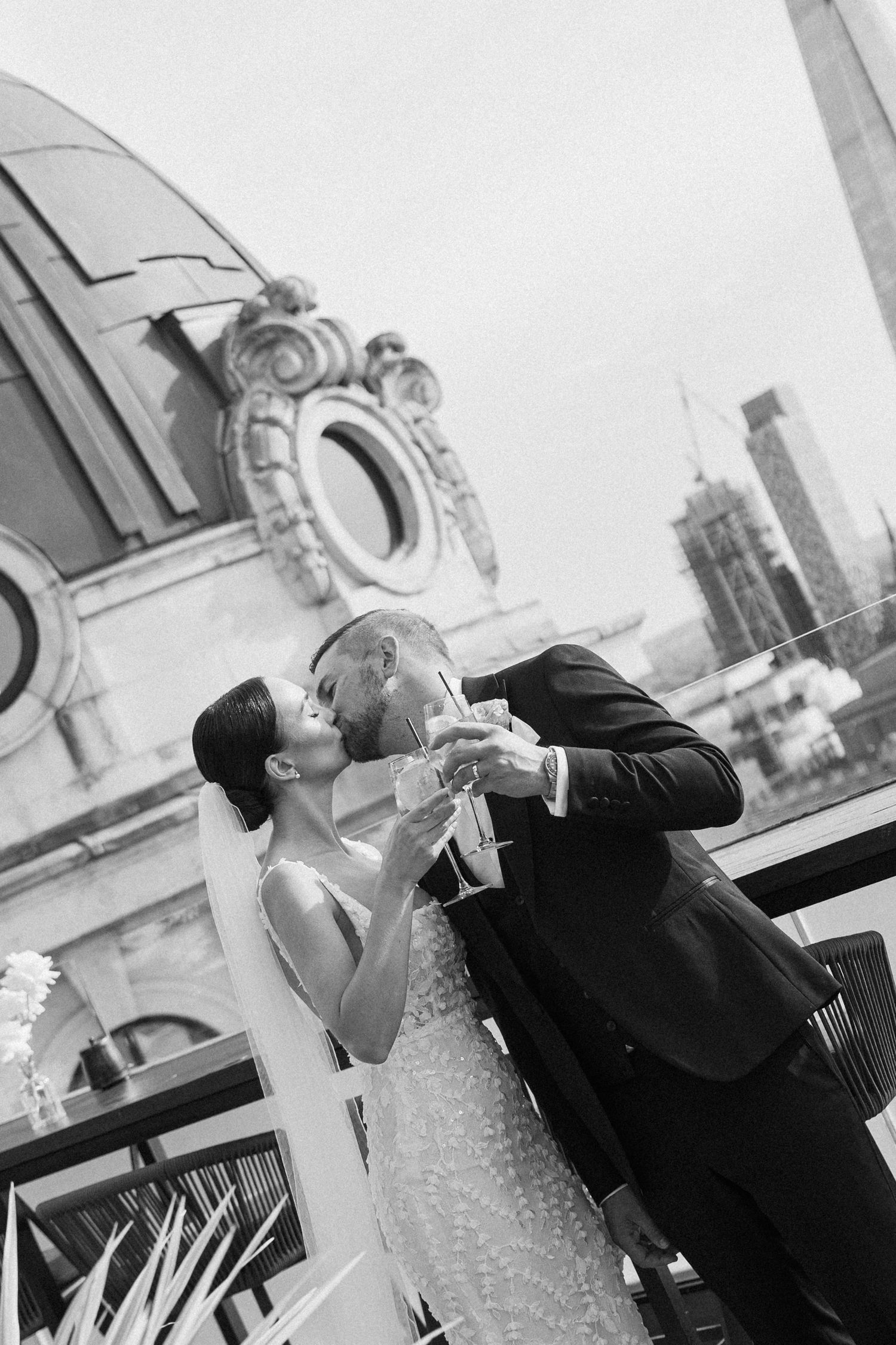 A black and white photo captures a couple toasting champagne with architectural details in the background.
