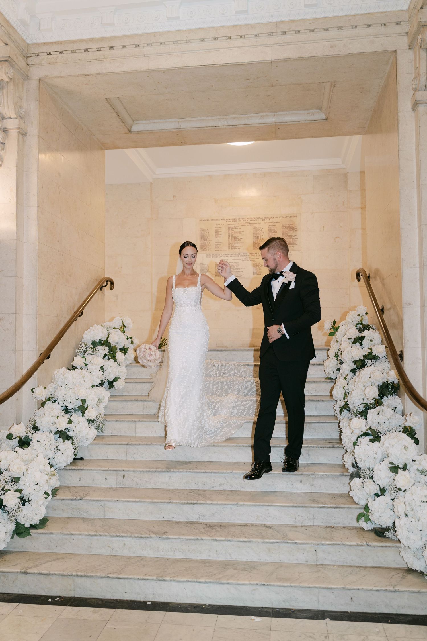 Wedding couple poses on decorated staircase with white floral arrangements.