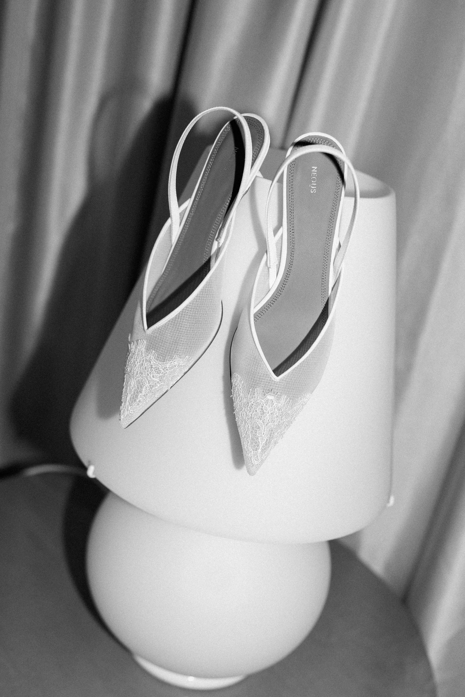 Elegant white bridal shoes photographed in dramatic black and white lighting.
