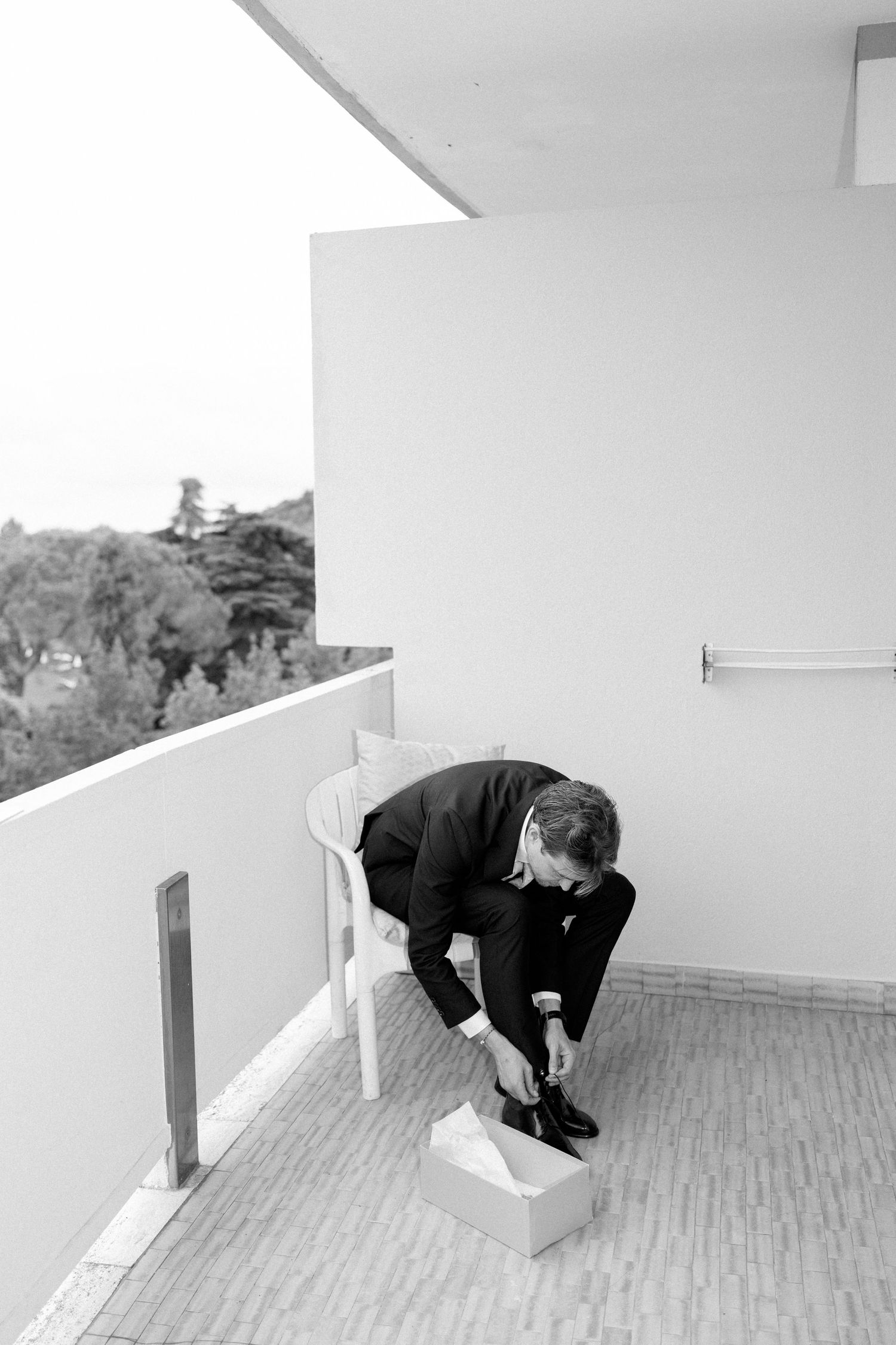 Person in dark suit crouching on outdoor deck or balcony.