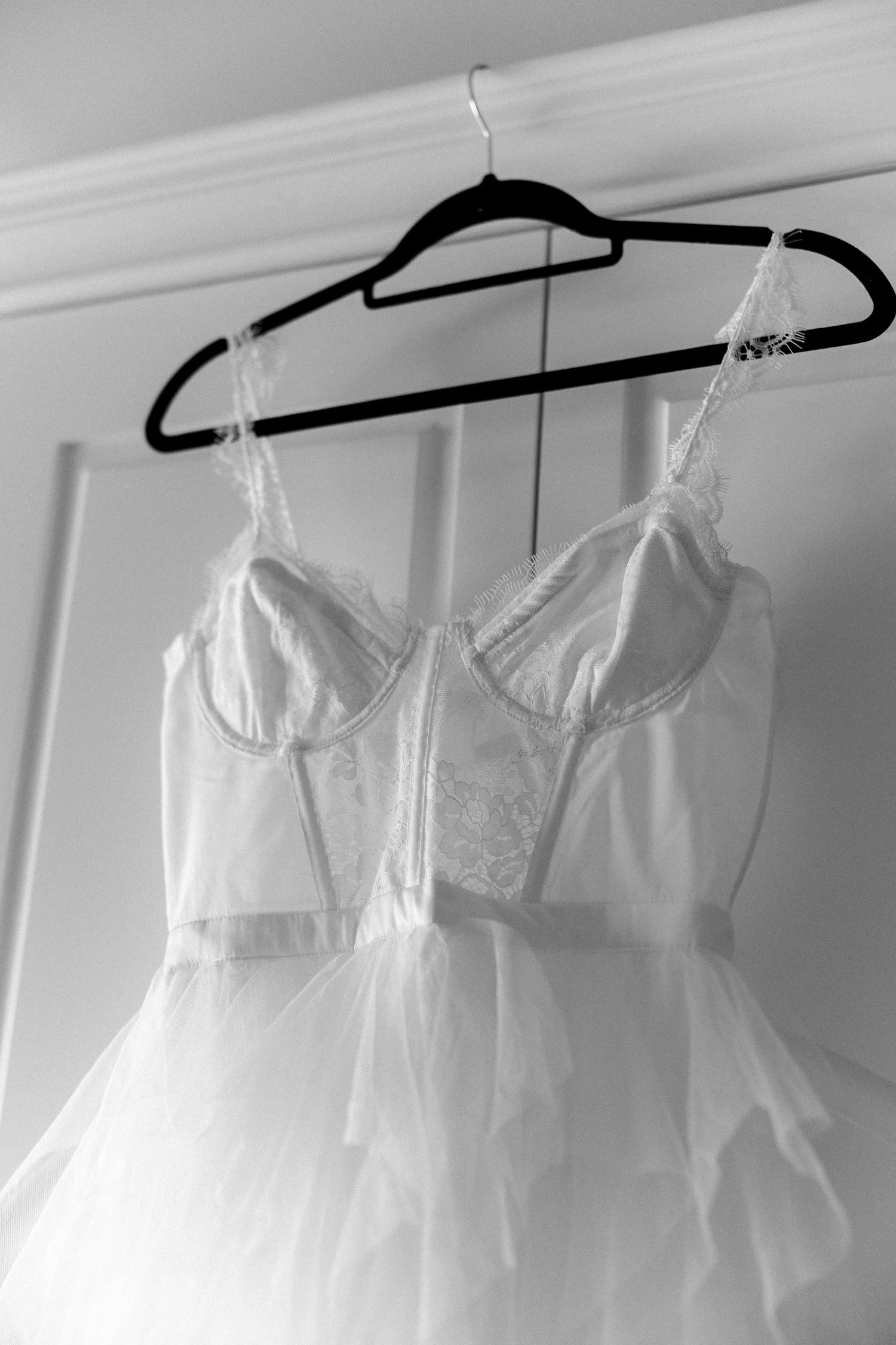 Close-up of white wedding dress bodice with lace details hanging on black hanger.