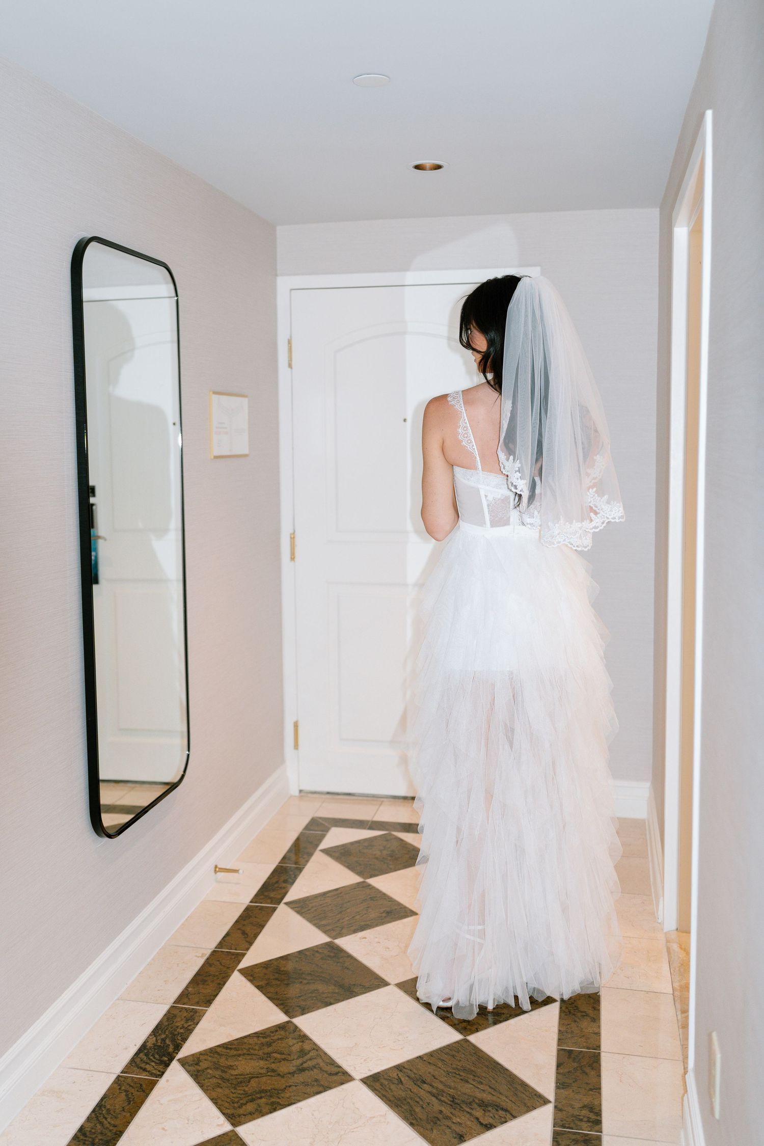 Back view of bride in layered tulle dress standing in modern hallway.