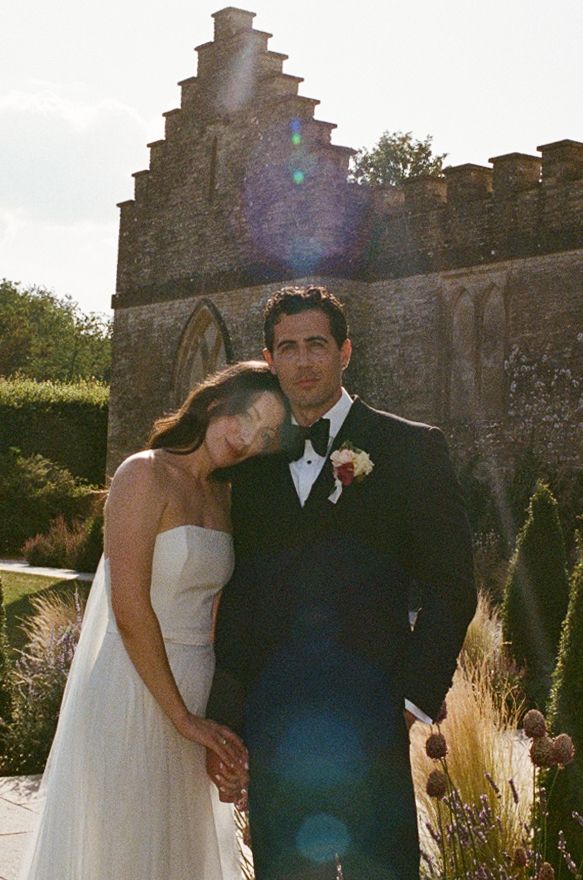 Bride and groom pose together in front of a historic stone castle wall during their outdoor wedding ceremony.