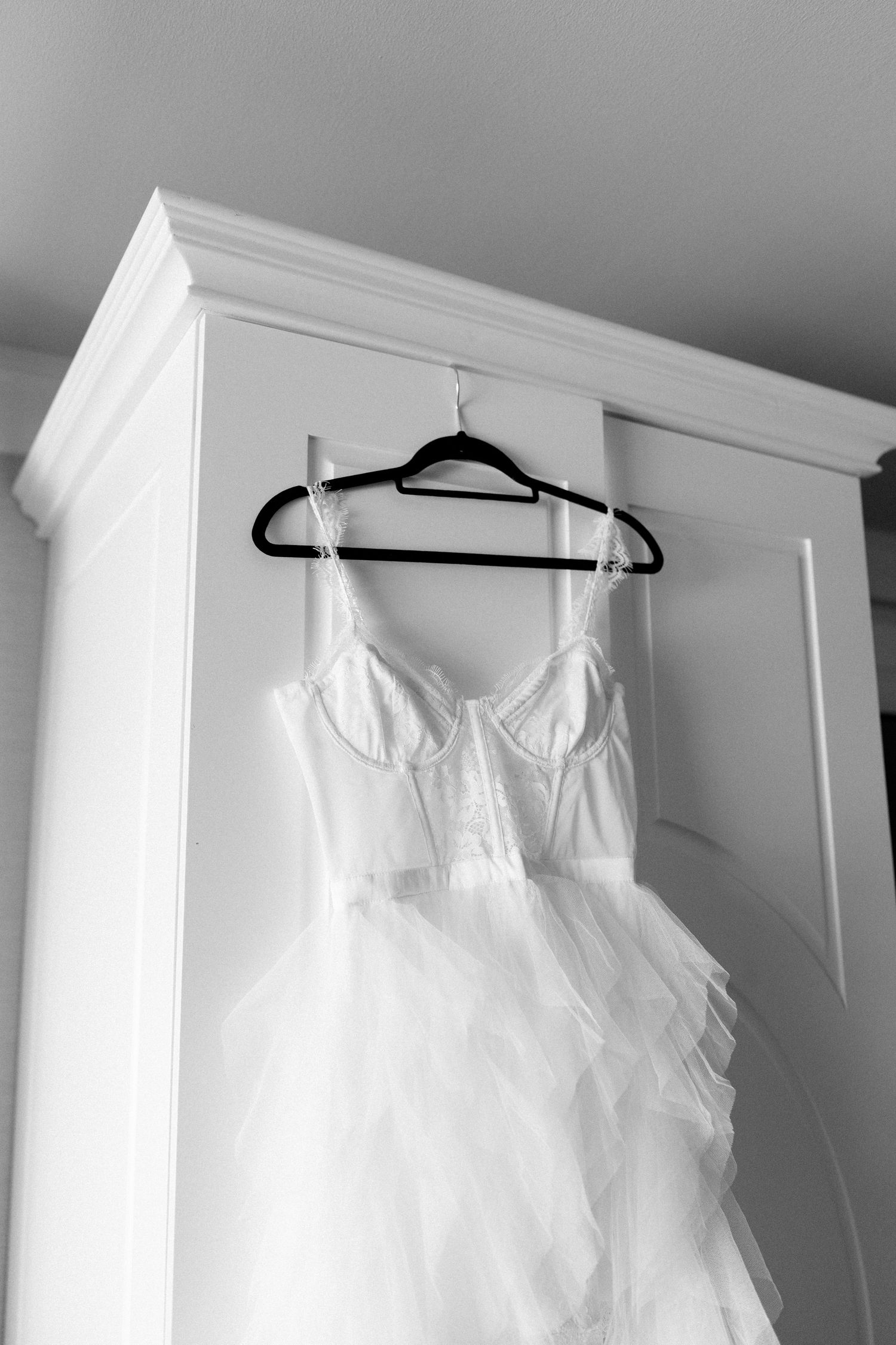 White wedding dress hanging on black hanger against white wardrobe door.
