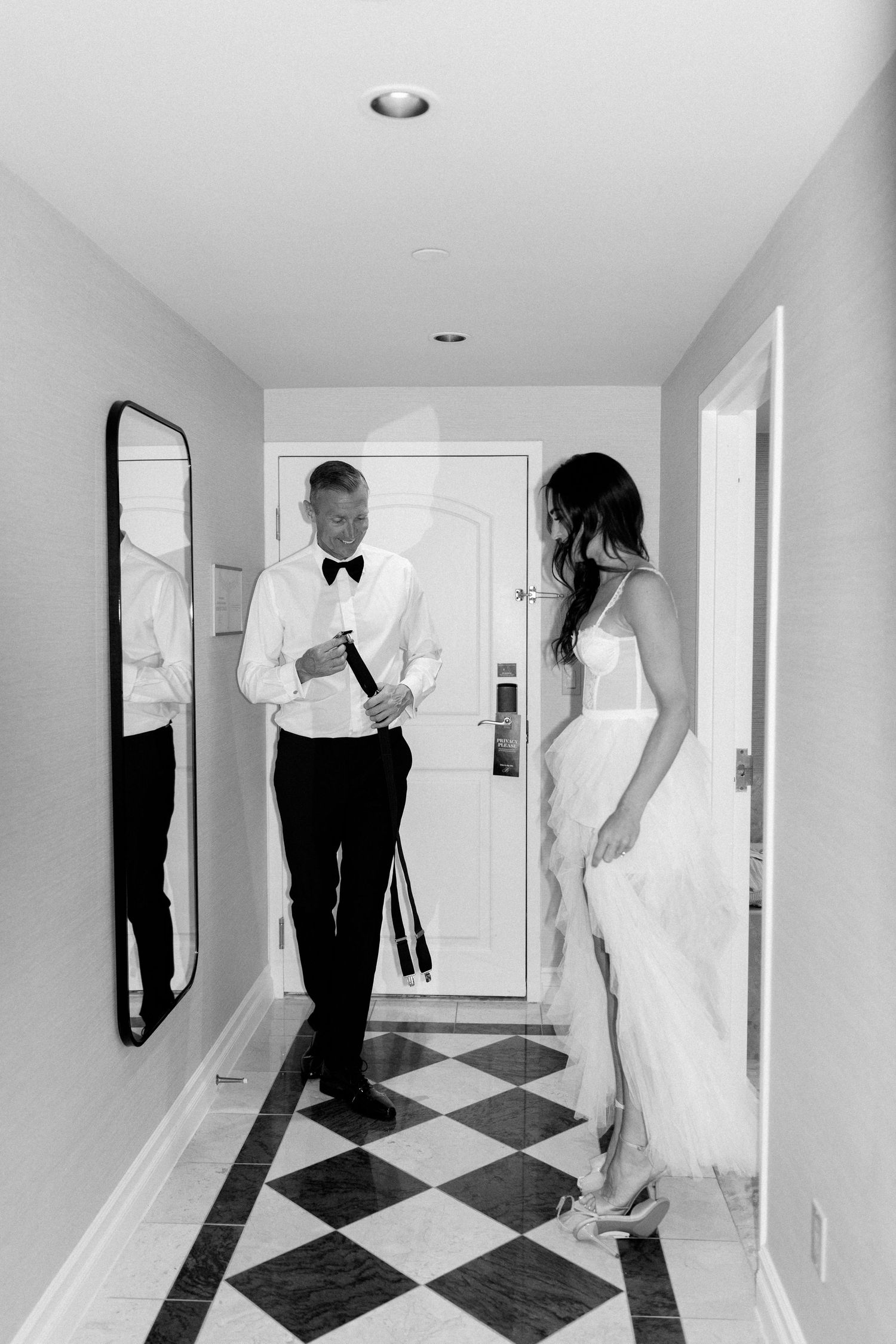 Elegant couple in formal attire standing in a hallway with checkered flooring.