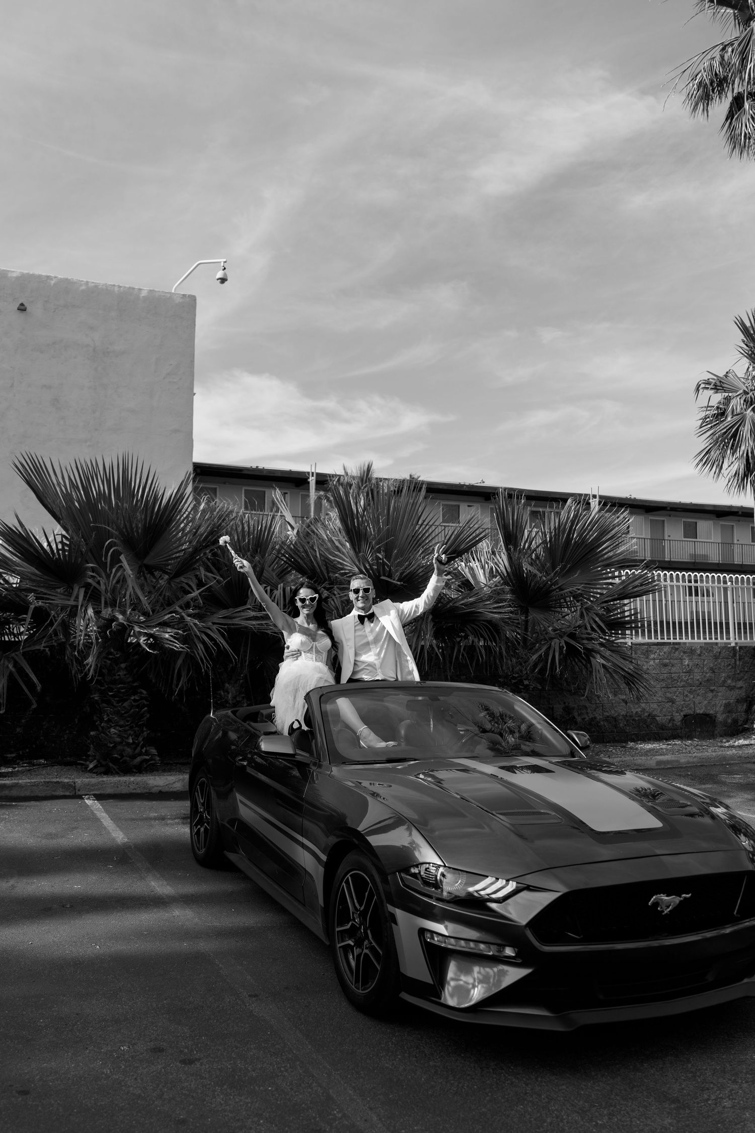 Black and white photo of newlyweds celebrating in a modern sports car.