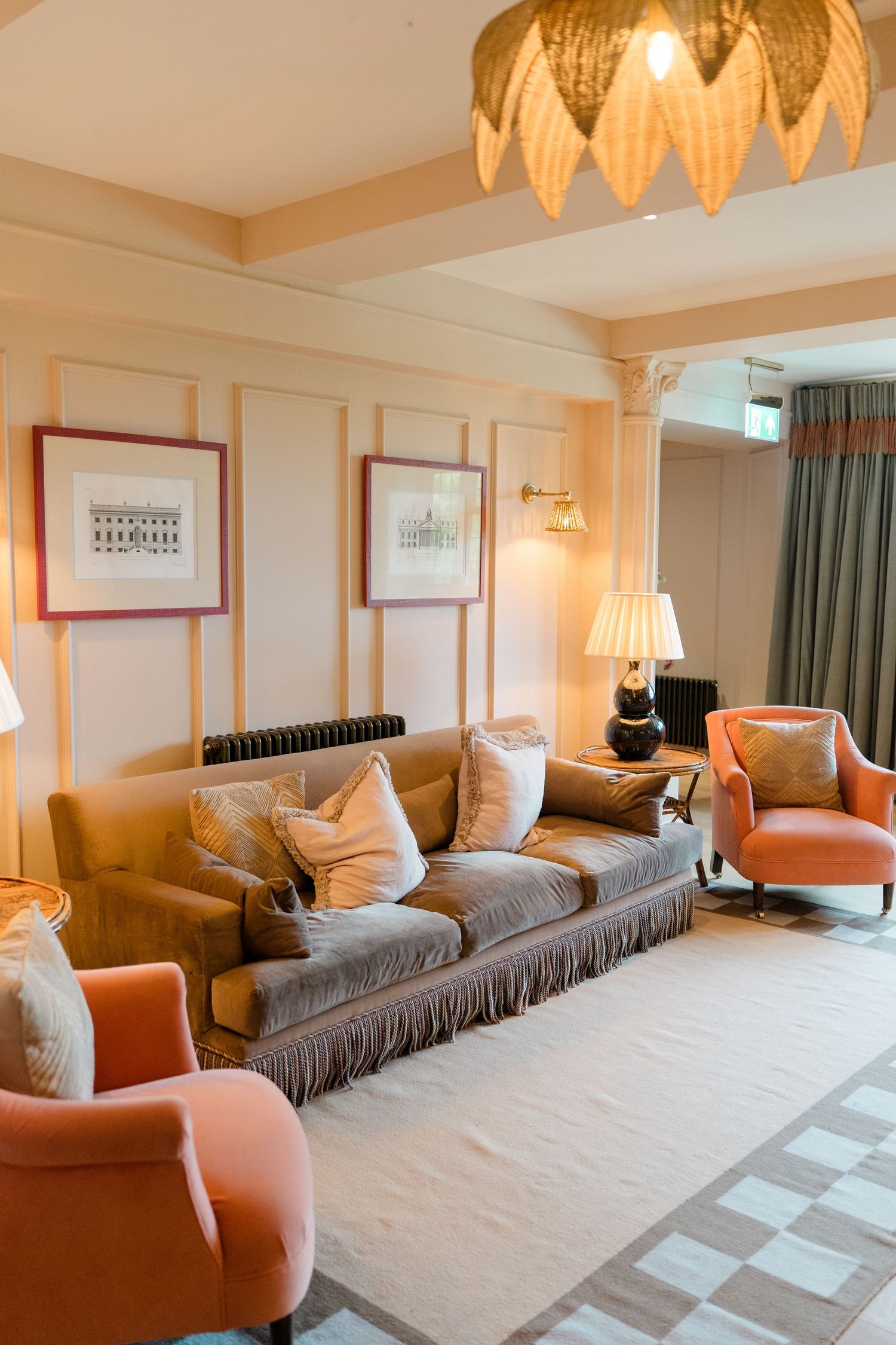 Elegant hotel suite living room with gray fringed sofa, coral armchairs, gold chandelier, and warm neutral decor.
