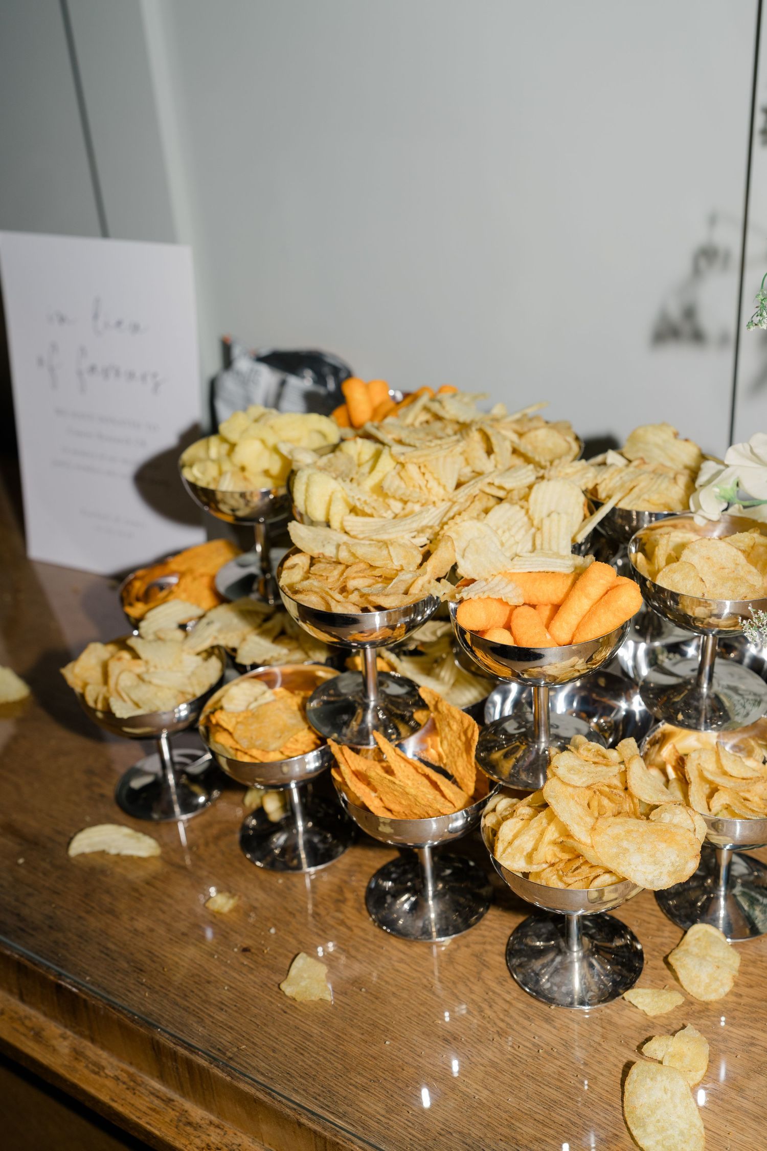 An elegant wedding snack display featuring assorted crisps and chips arranged in silver coupe glasses.