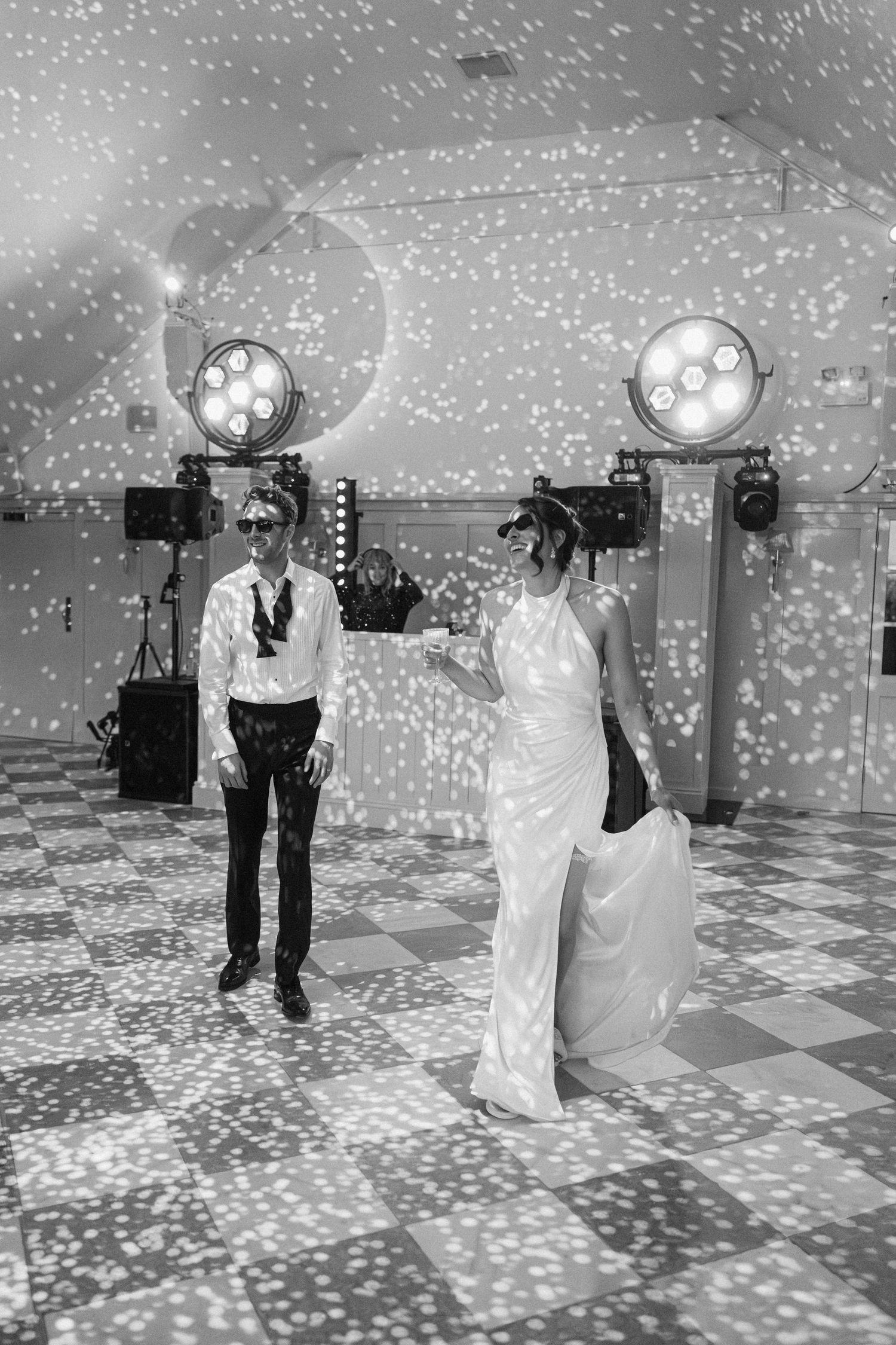 Bride and groom dance under starry light projections on a checkered floor wearing sunglasses.