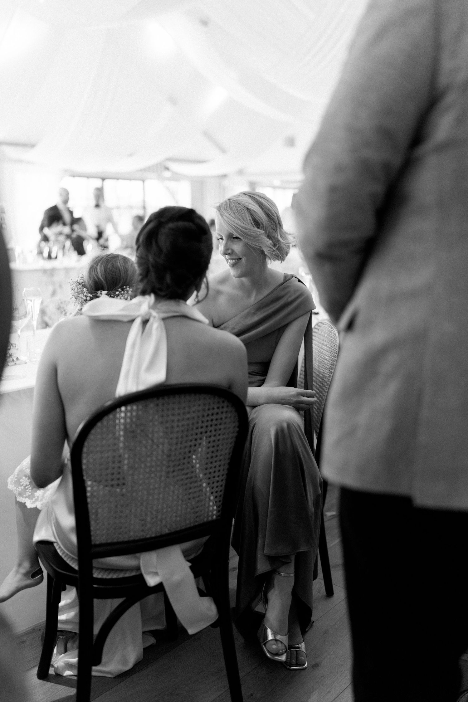 Black and white photo of smiling bridesmaid chatting with bride at wedding reception table.