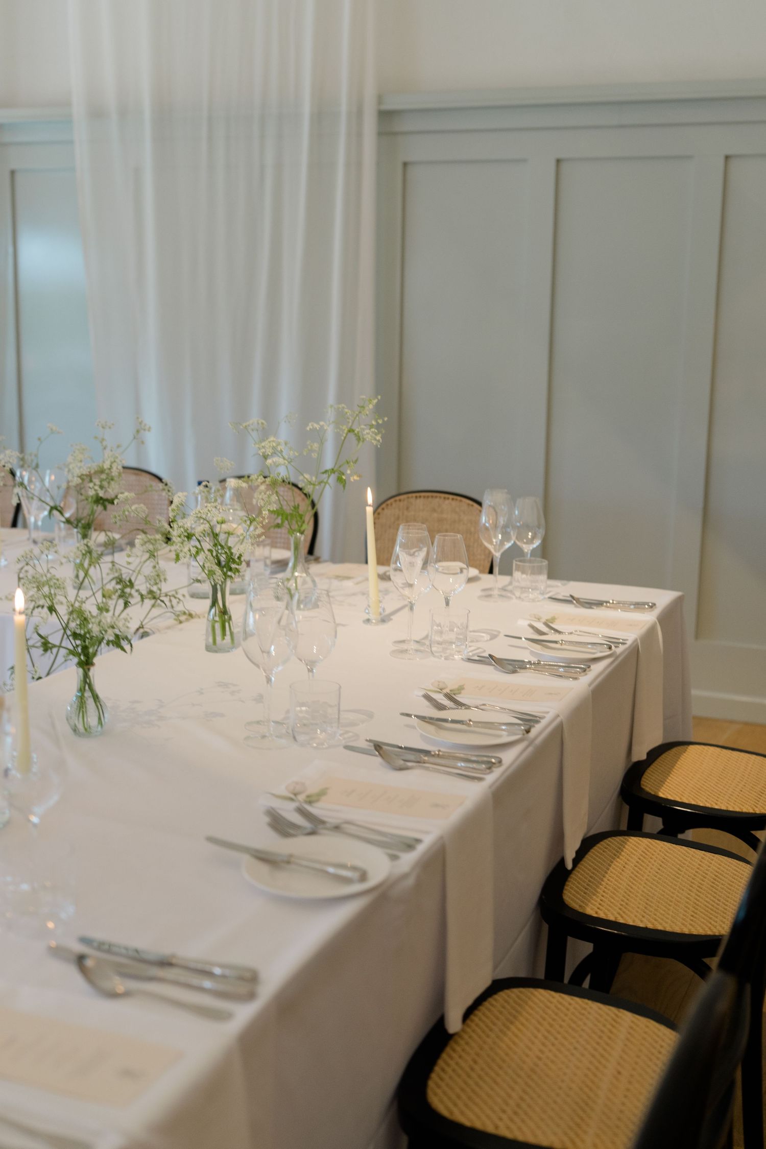 Elegant wedding reception table set with white linens, candles, glassware, and delicate floral arrangements.