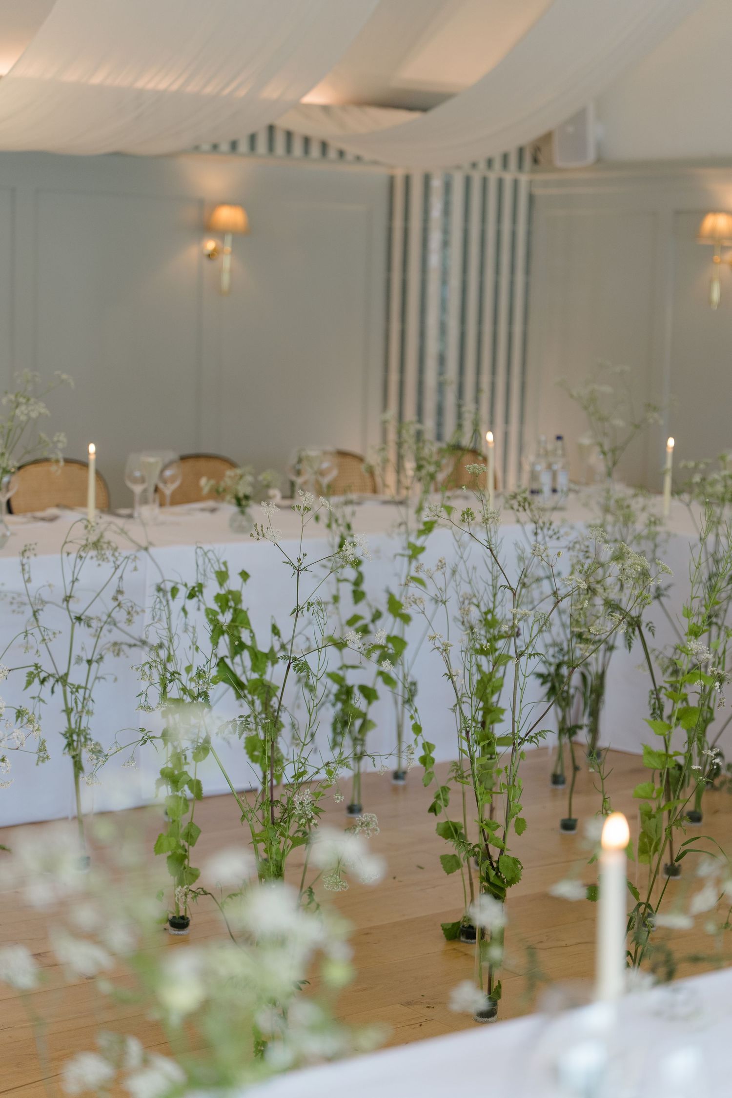 Elegant wedding reception hall decorated with tall green botanical centerpieces and white candles.