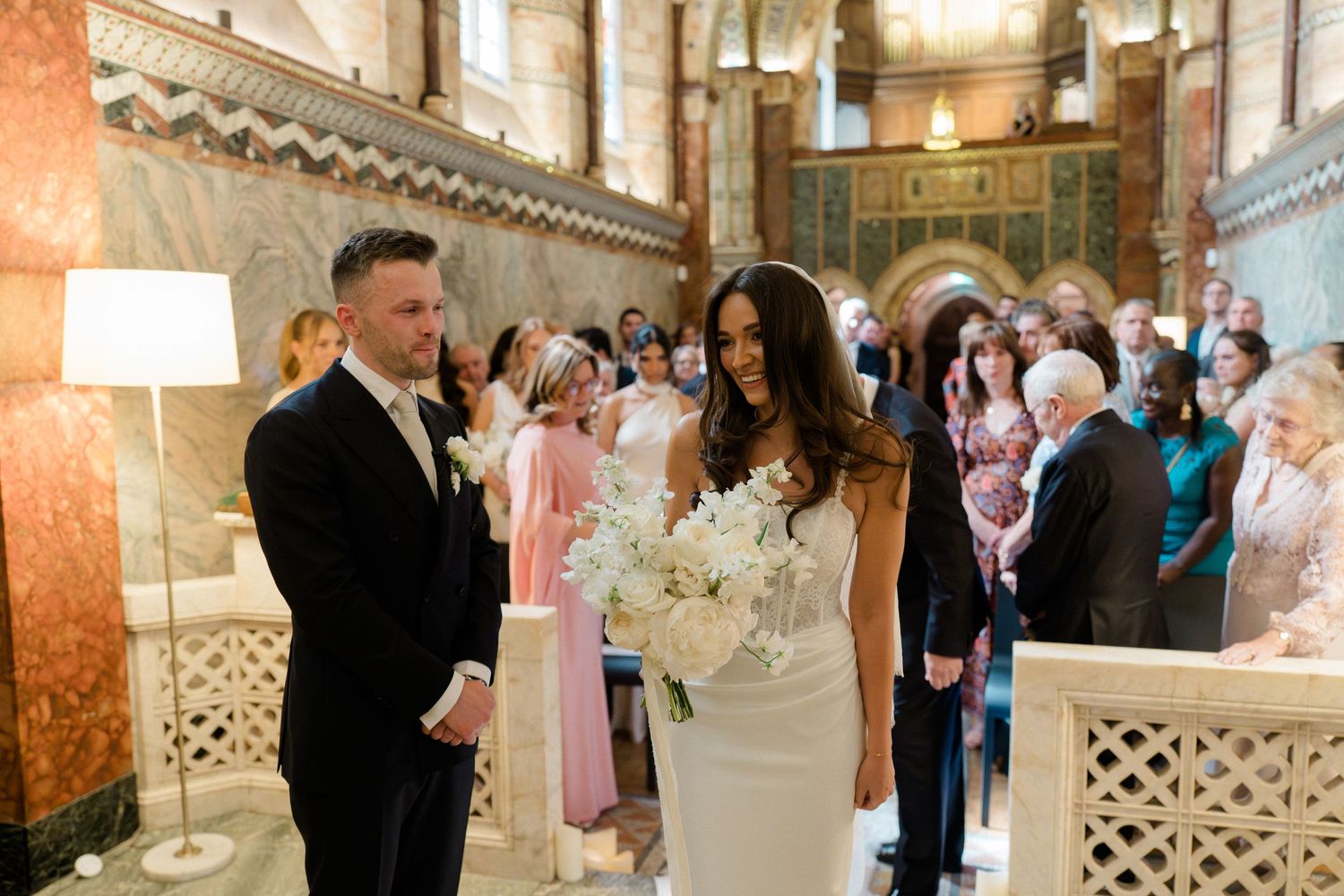 Bride and groom stand at the altar during an elegant wedding ceremony in a grand ornate venue.