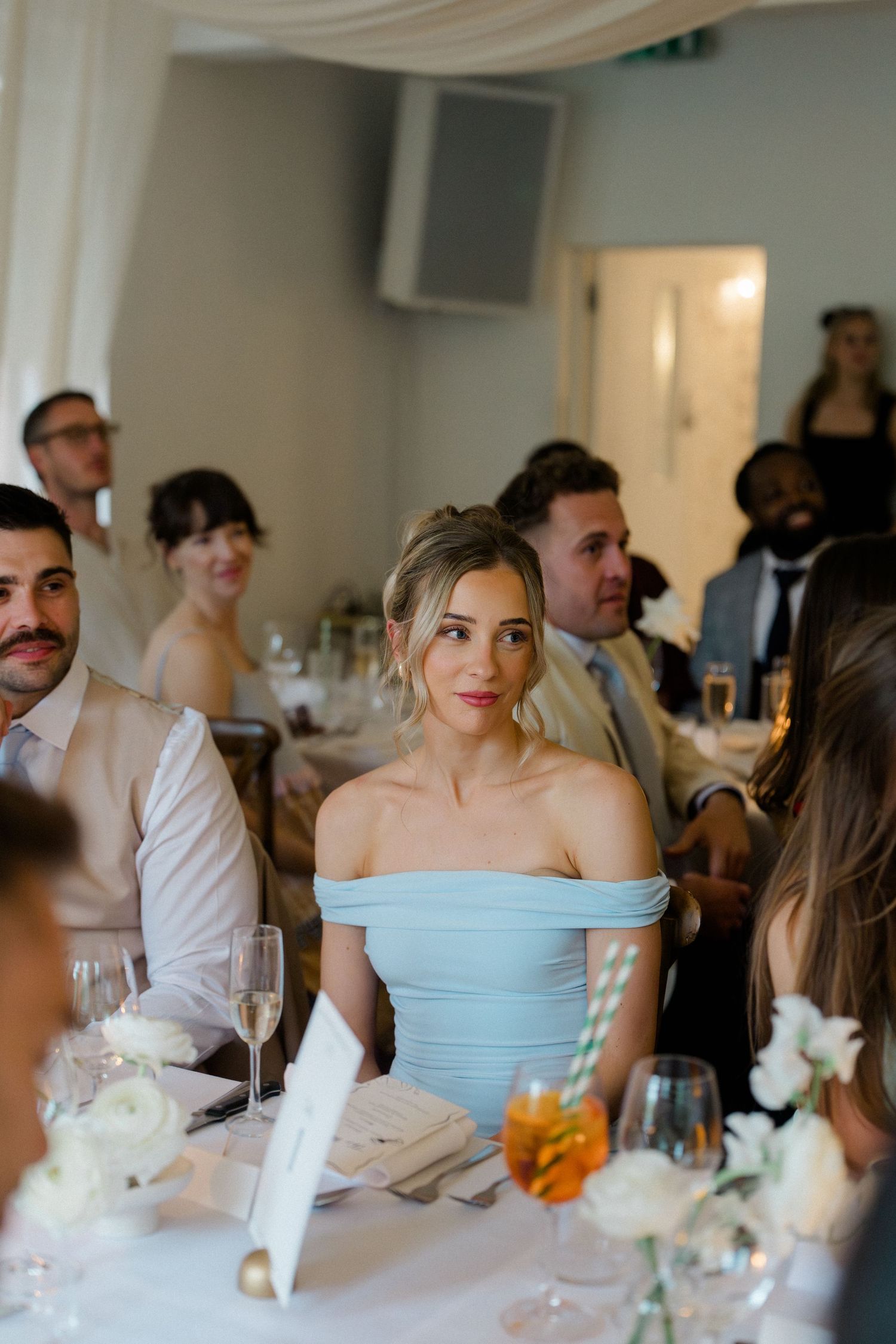 Elegant bridesmaid in light blue off-shoulder gown seated at a decorated wedding reception dinner table.