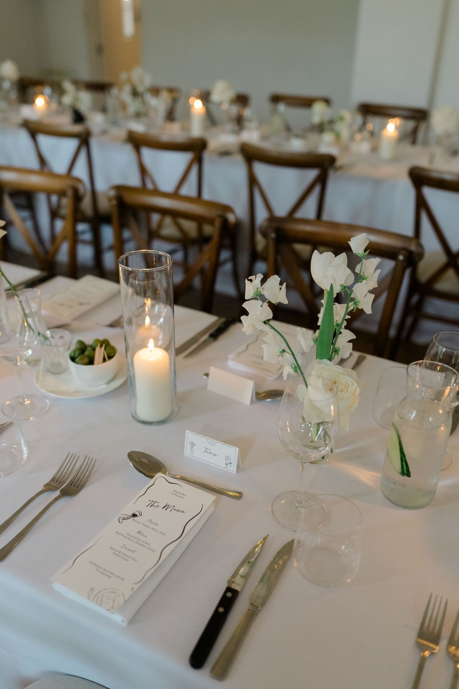Sophisticated wedding reception table set with white flowers, candles, menus and gold cutlery.