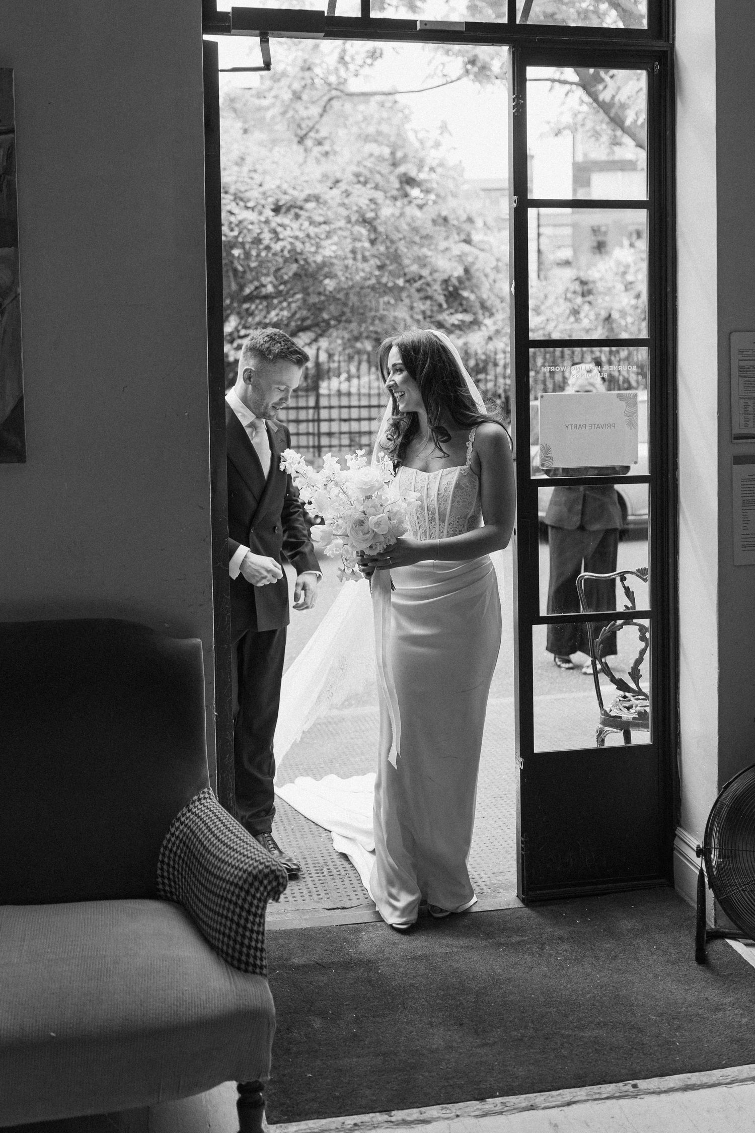 Black and white photo of bride and groom standing in a doorway with natural light.