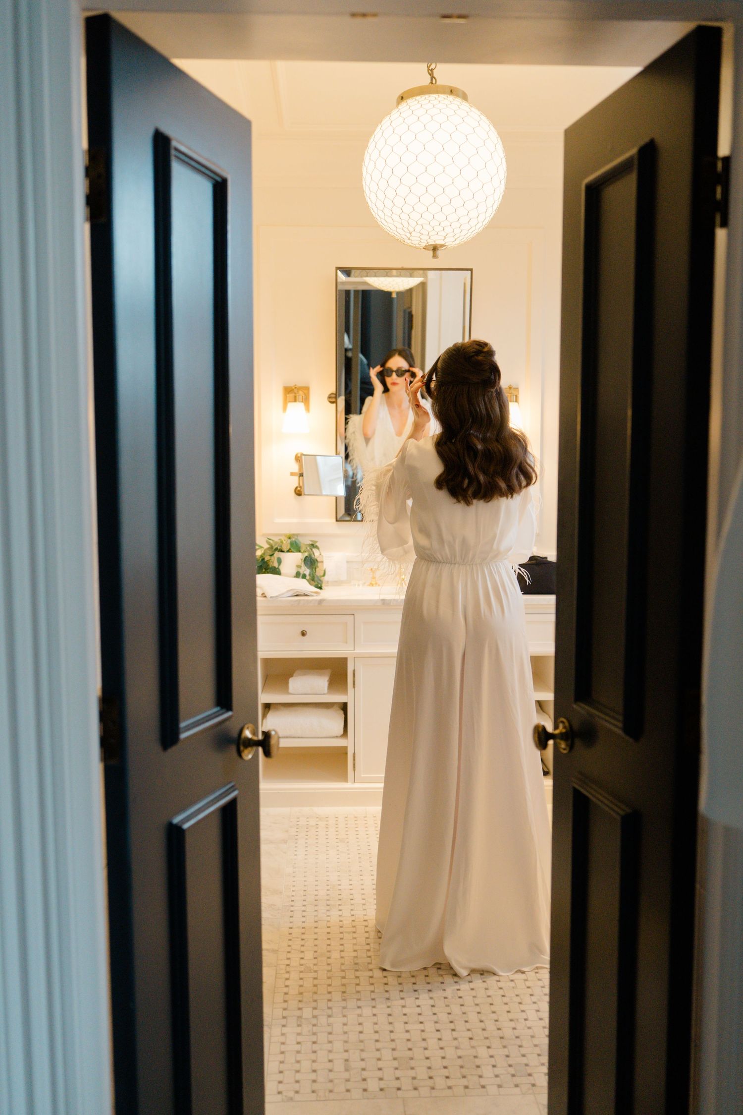 Bride in white robe preparing in elegant bathroom mirror before wedding.