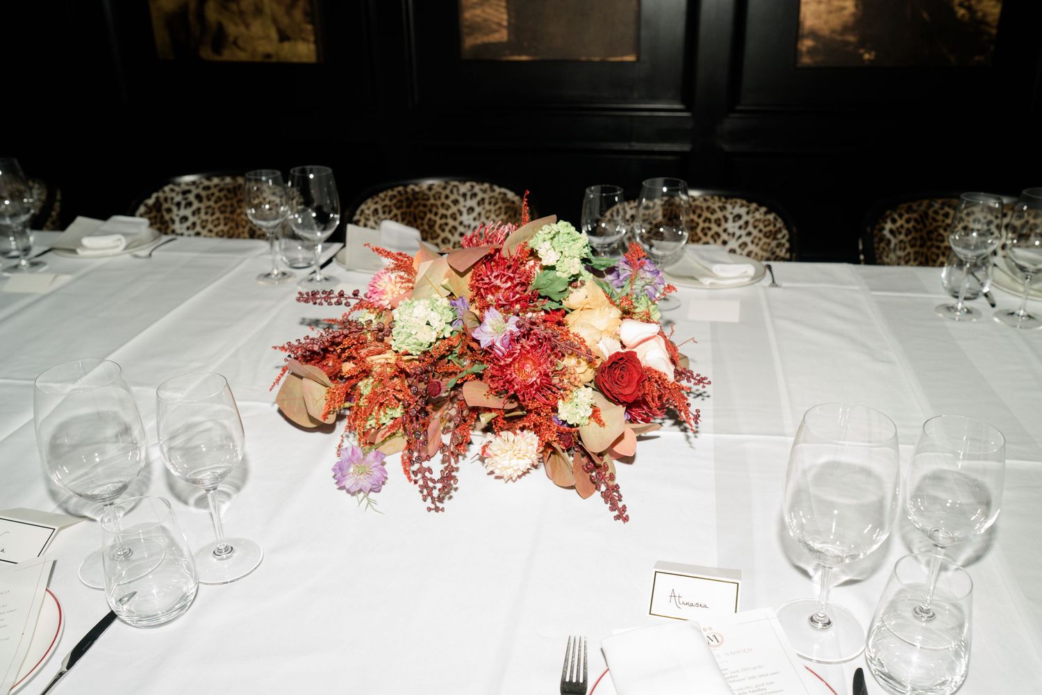 Colorful floral centerpiece with roses and wildflowers on white tablecloth at wedding reception.
