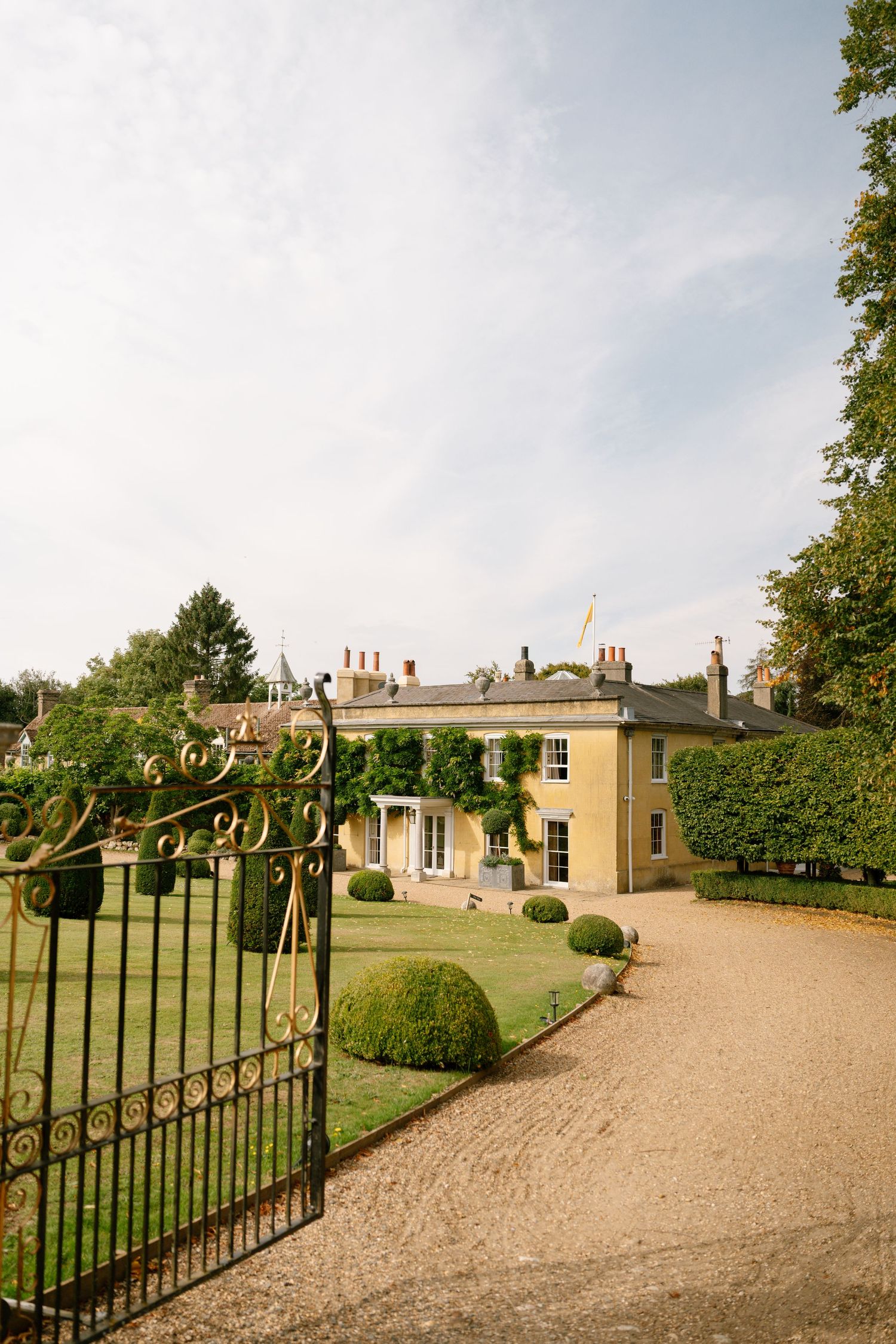 Wrought iron gates leading to a stately yellow manor house with circular driveway.