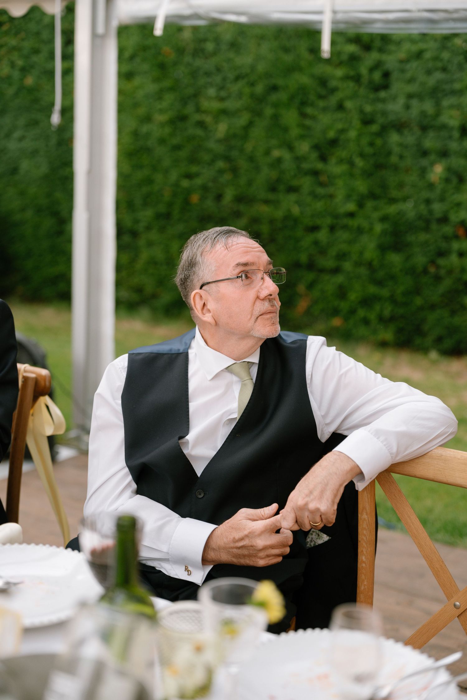 Guest relaxing in wooden chair during outdoor wedding reception.