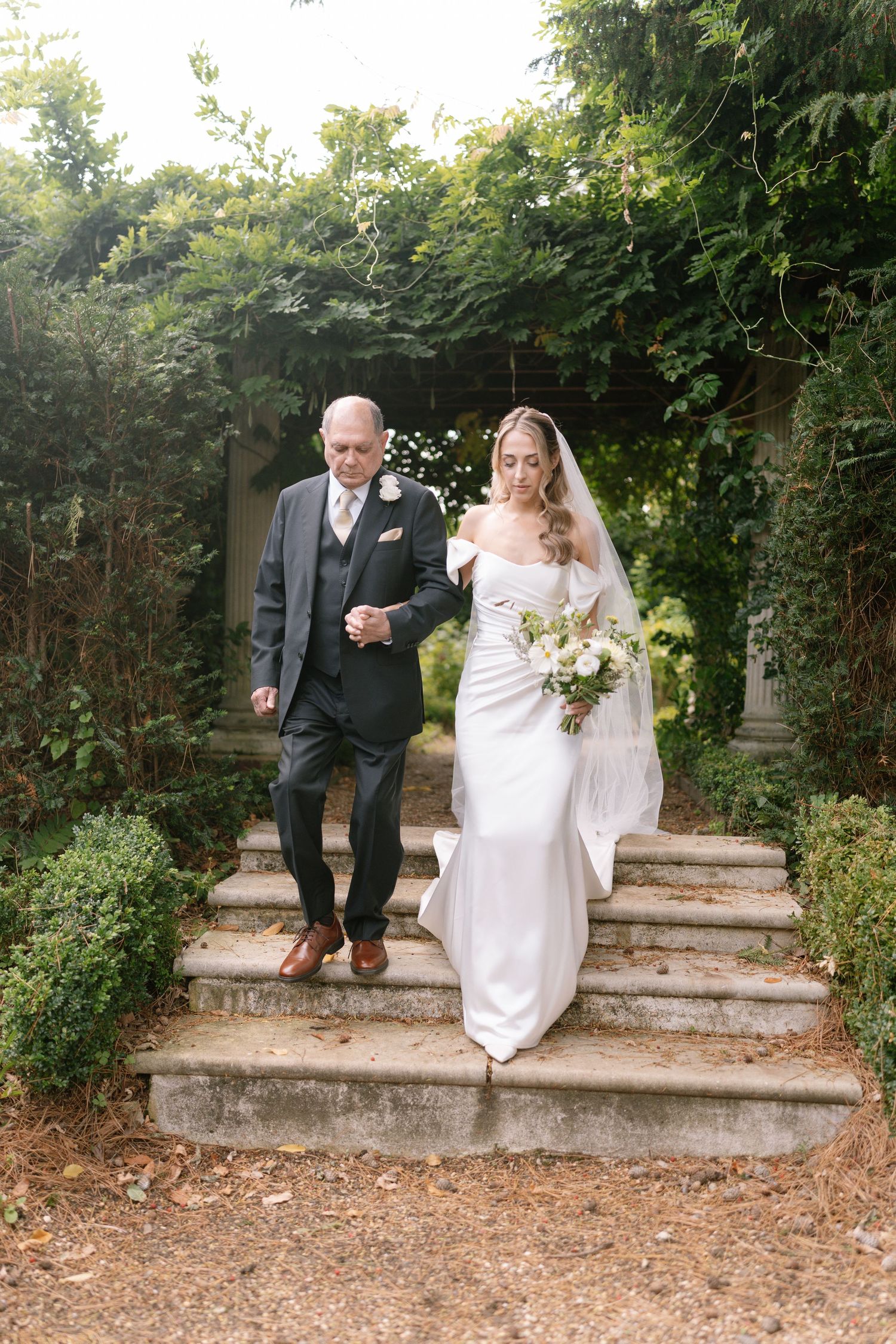 Wedding party navigating stone steps in a lush garden setting.