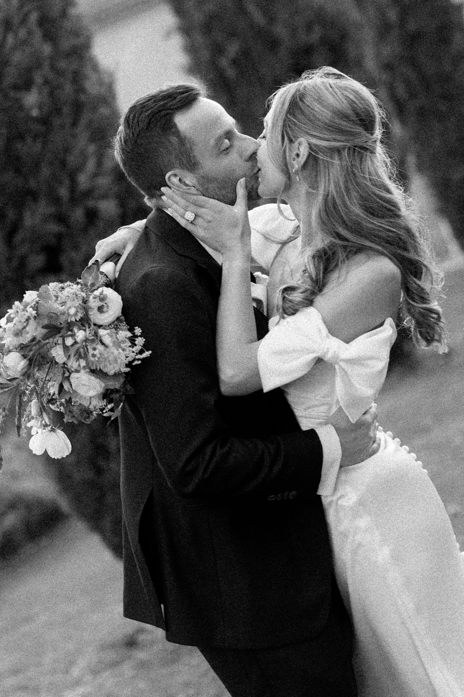 A black and white wedding photo capturing an intimate moment in a garden setting.