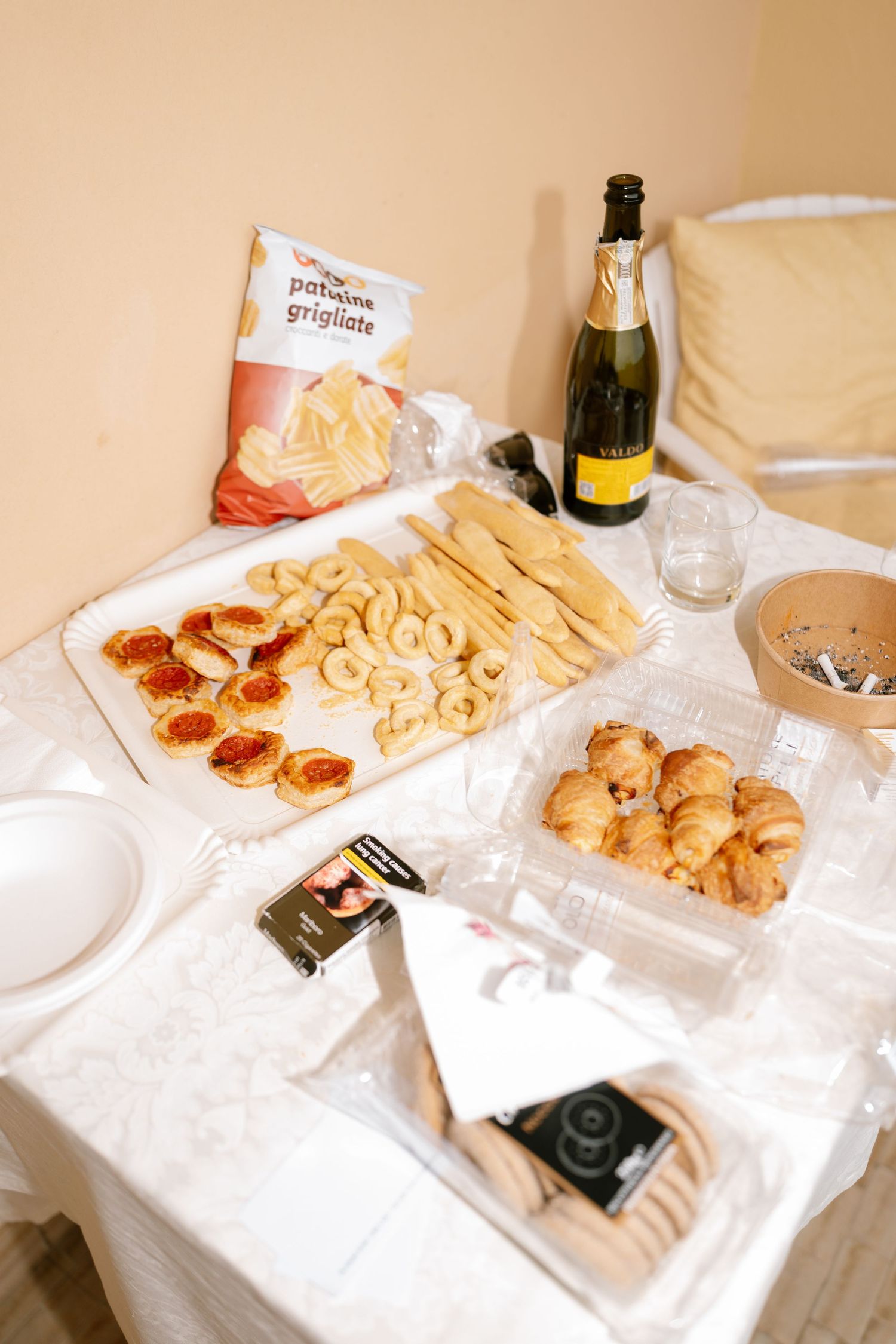 Snacks and appetizers laid out on white tablecloth with wine bottles.