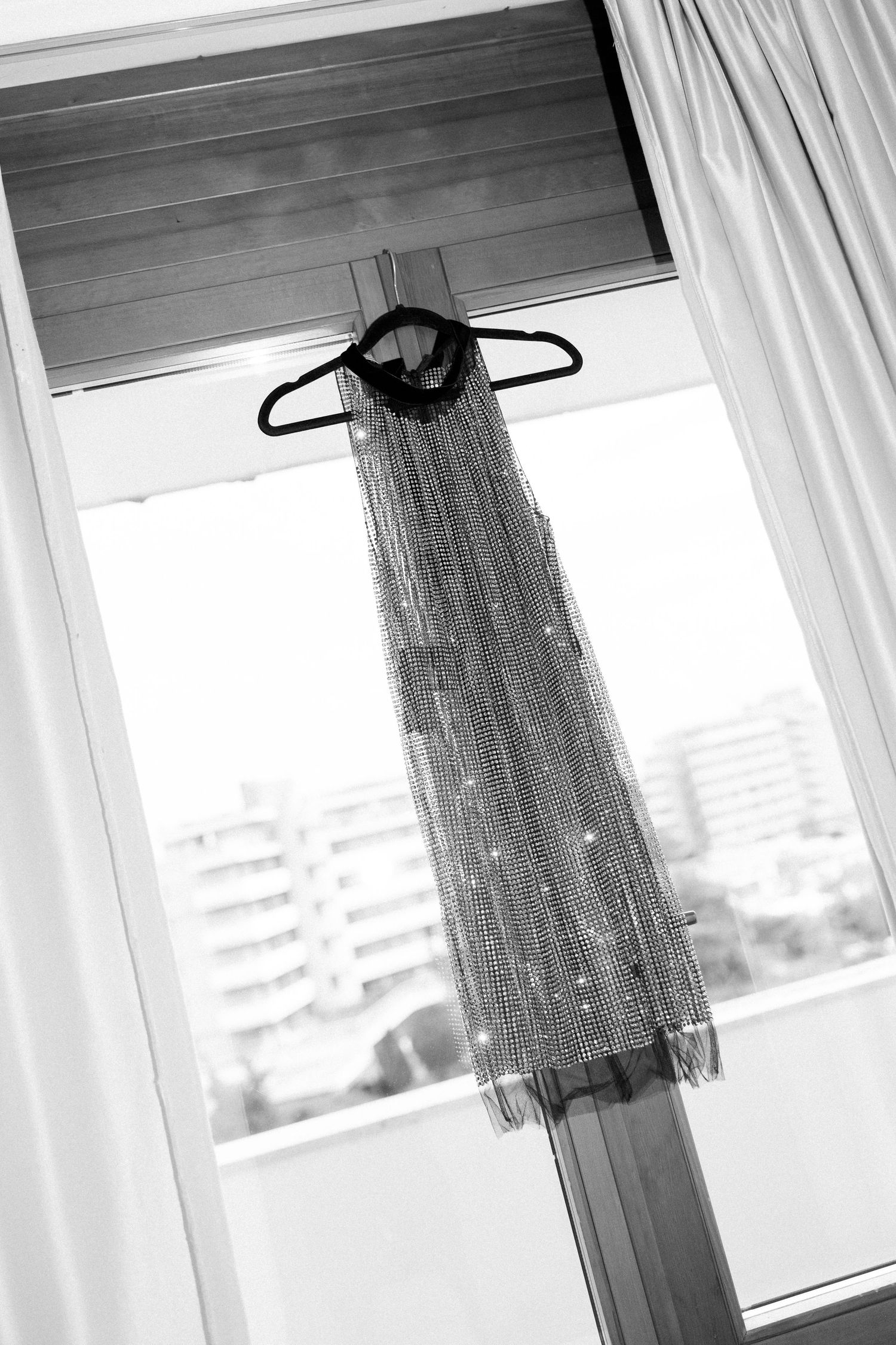White curtains and dresses hanging by windows with city view in black and white.