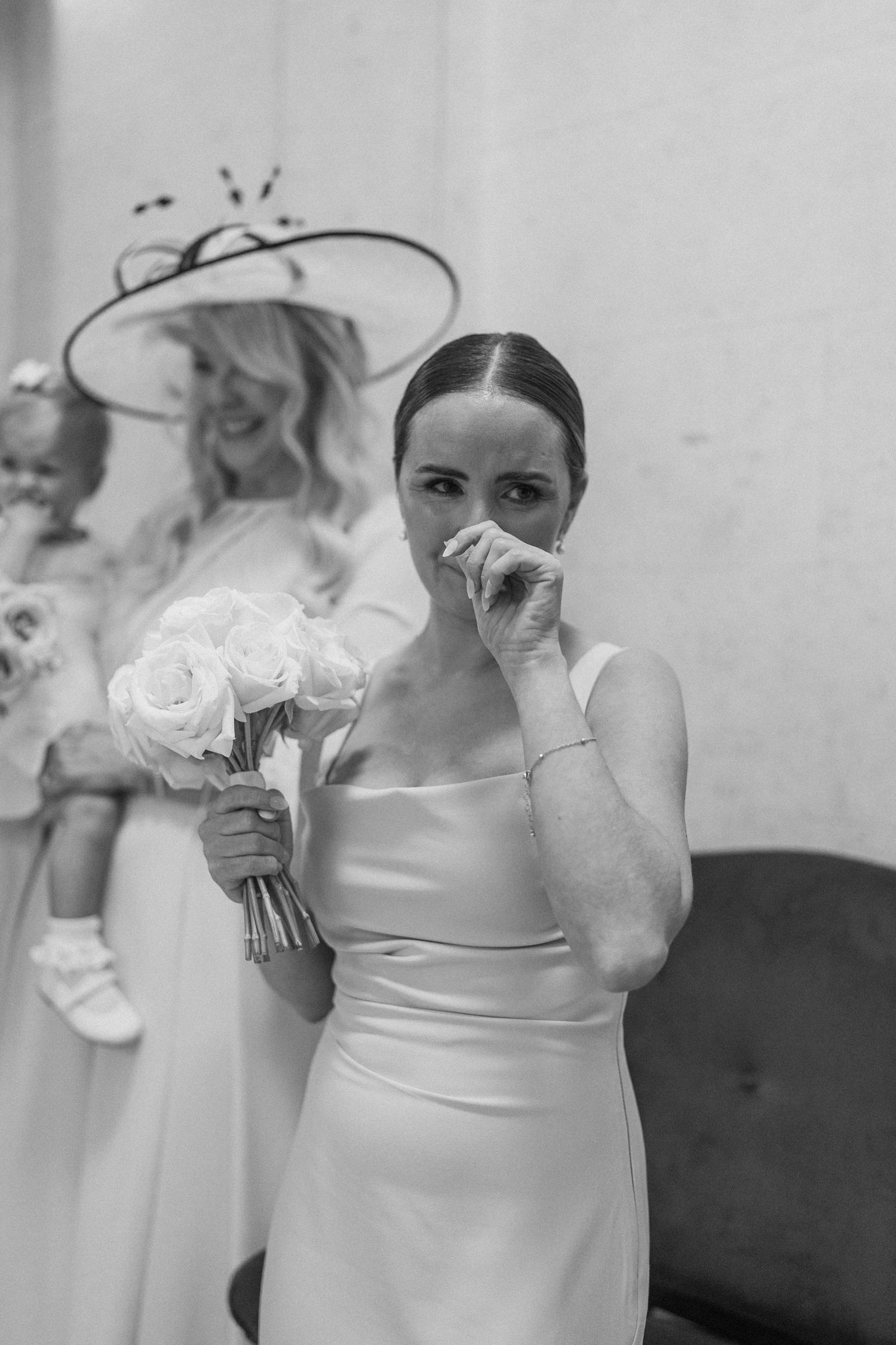 An emotional moment captured in black and white as attendant holds bouquet during wedding ceremony.
