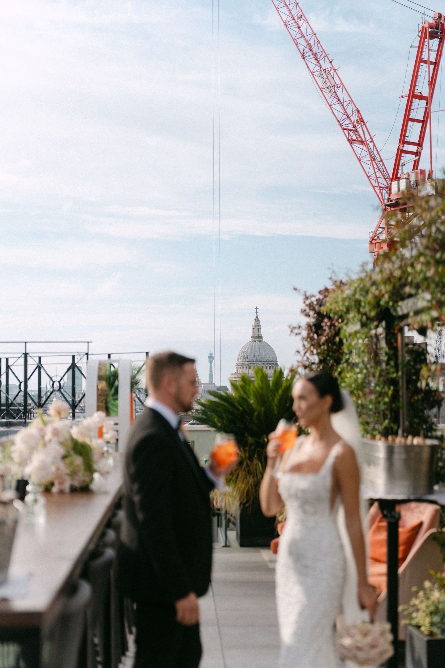 A wedding couple shares a romantic moment on a rooftop terrace with construction cranes visible in the background.